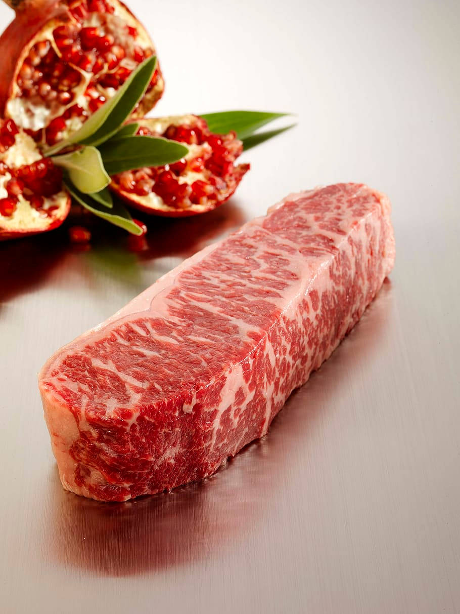 拉絲金屬表面上的大理石紋牛肉扒配石榴和綠葉