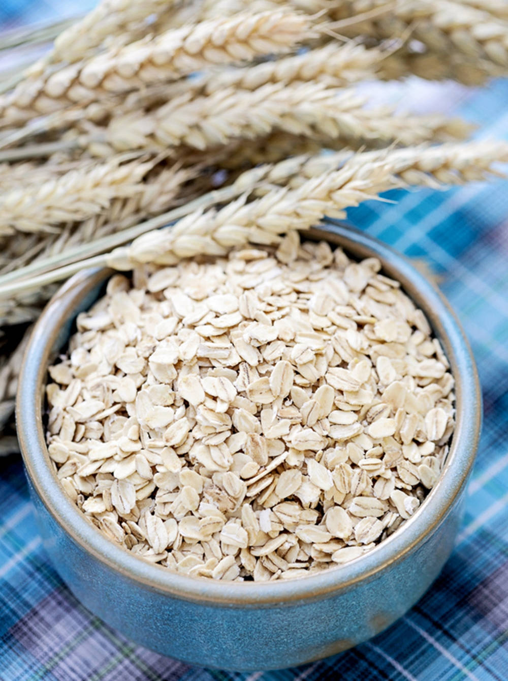 新鮮壓扁燕麥 壁紙 — 一個質樸的藍色陶瓷碗裝滿了燕麥片，旁邊是金色麥稈，放在格紋布上。