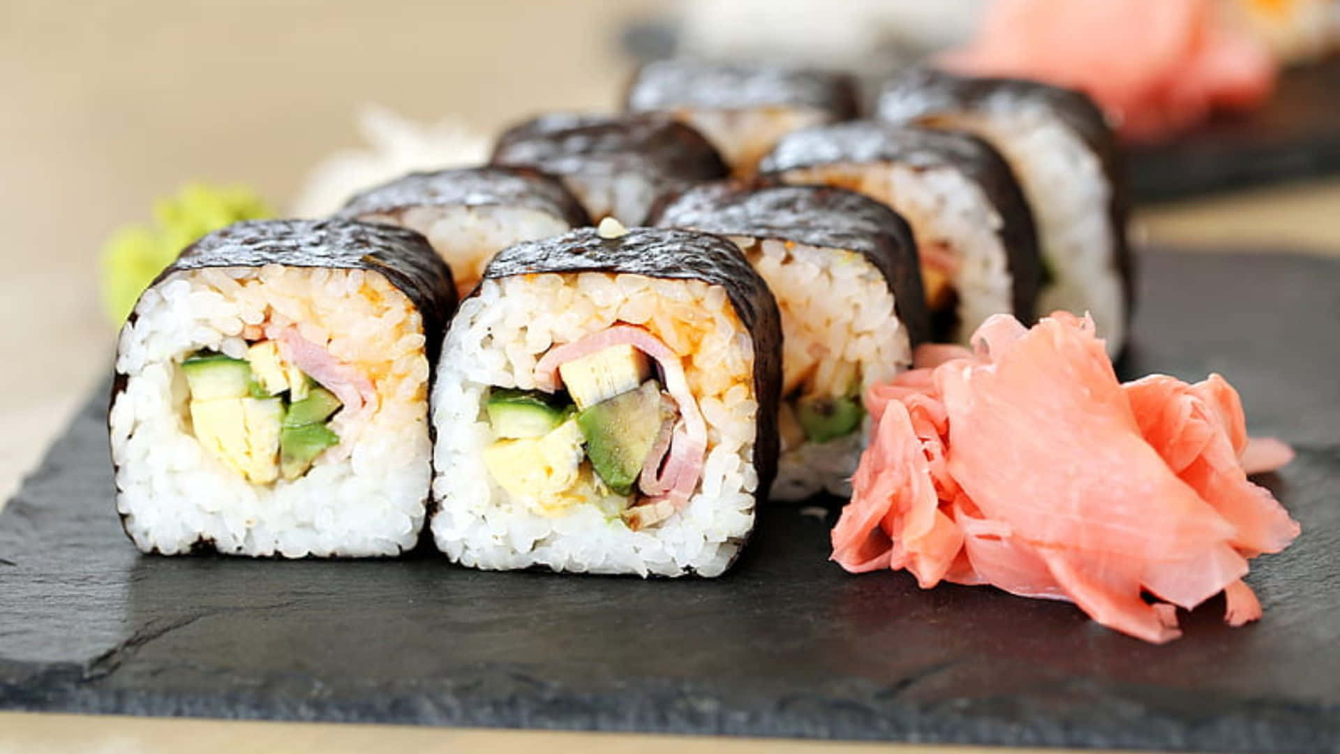 Sushi 桌布 壁紙 — 新鮮壽司卷配牛油果、雞蛋和火腿，整齊地放在石板碟上，旁邊有醃漬生薑。