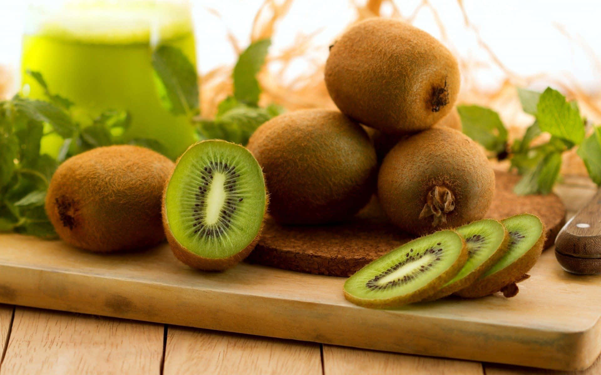 Kiwi 桌布 壁紙 — 新鮮奇異果切片及原個放在木板上，配以薄荷葉和一杯綠色果汁。