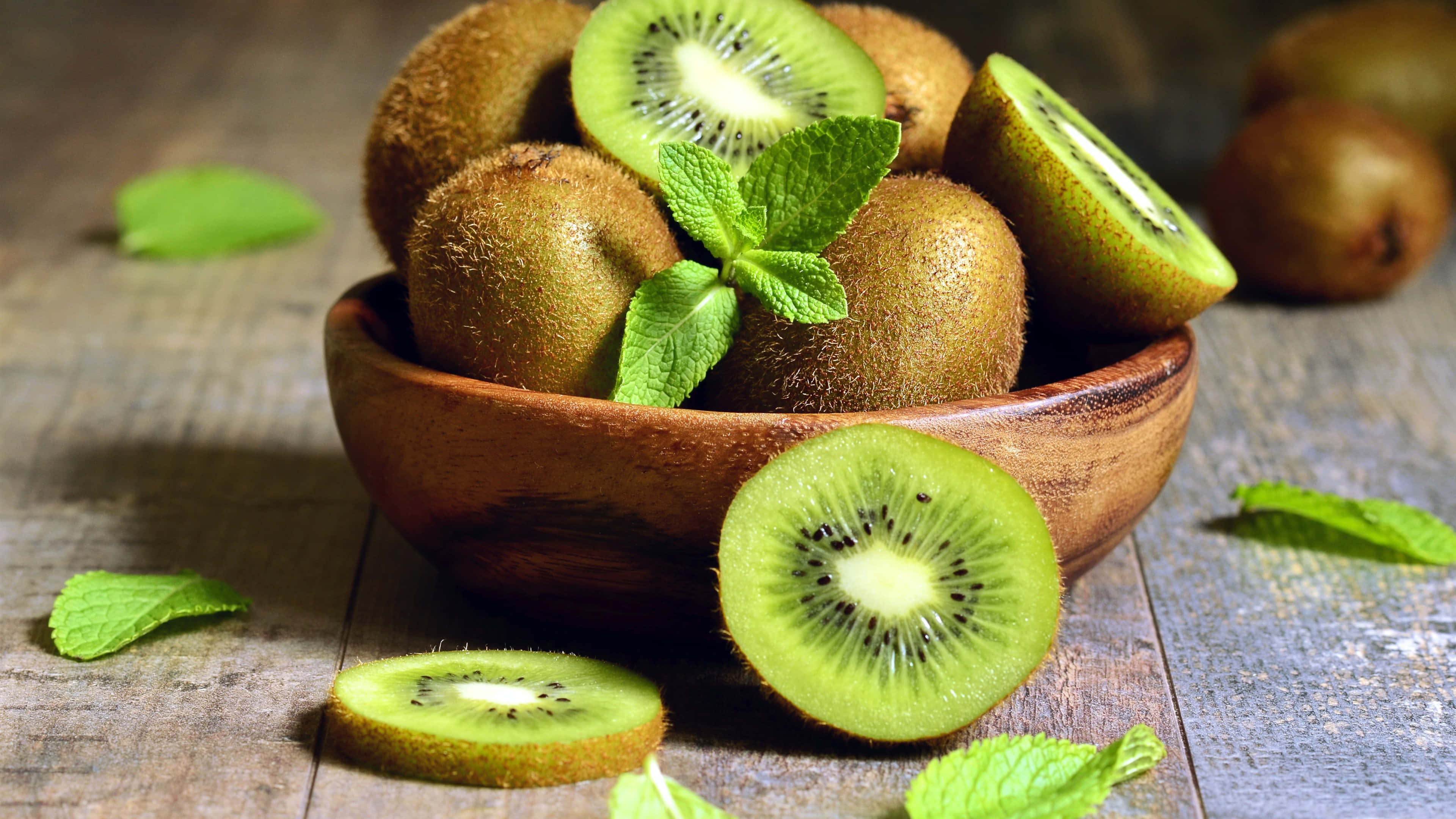 Kiwi 桌布 壁紙 — 新鮮奇異果放在木碗中，搭配薄荷葉，置於鄉村風木桌上。