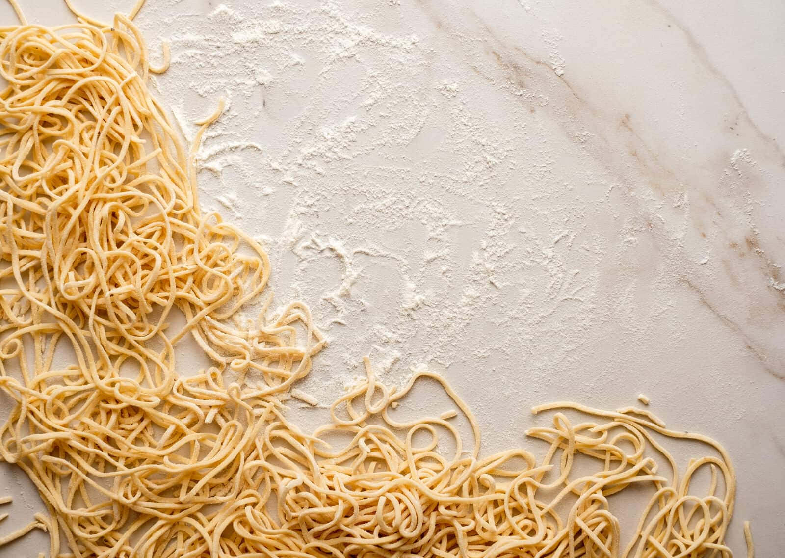 Noodles 桌布 壁紙 — 新鮮手工意大利麵條散落在撒滿麵粉的大理石檯面上。