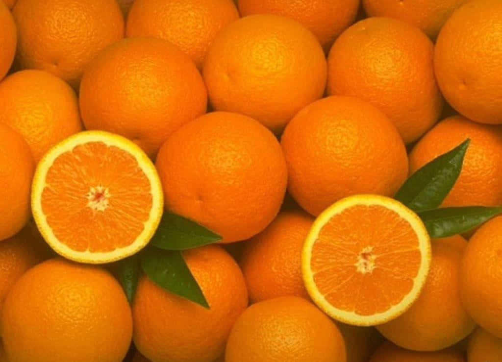 Orange Fruit 桌布 壁紙 — 新鮮橙嘅鮮豔近鏡，兩個切半嘅橙露出多汁嘅果瓣，綠色葉子喺完整水果之間。