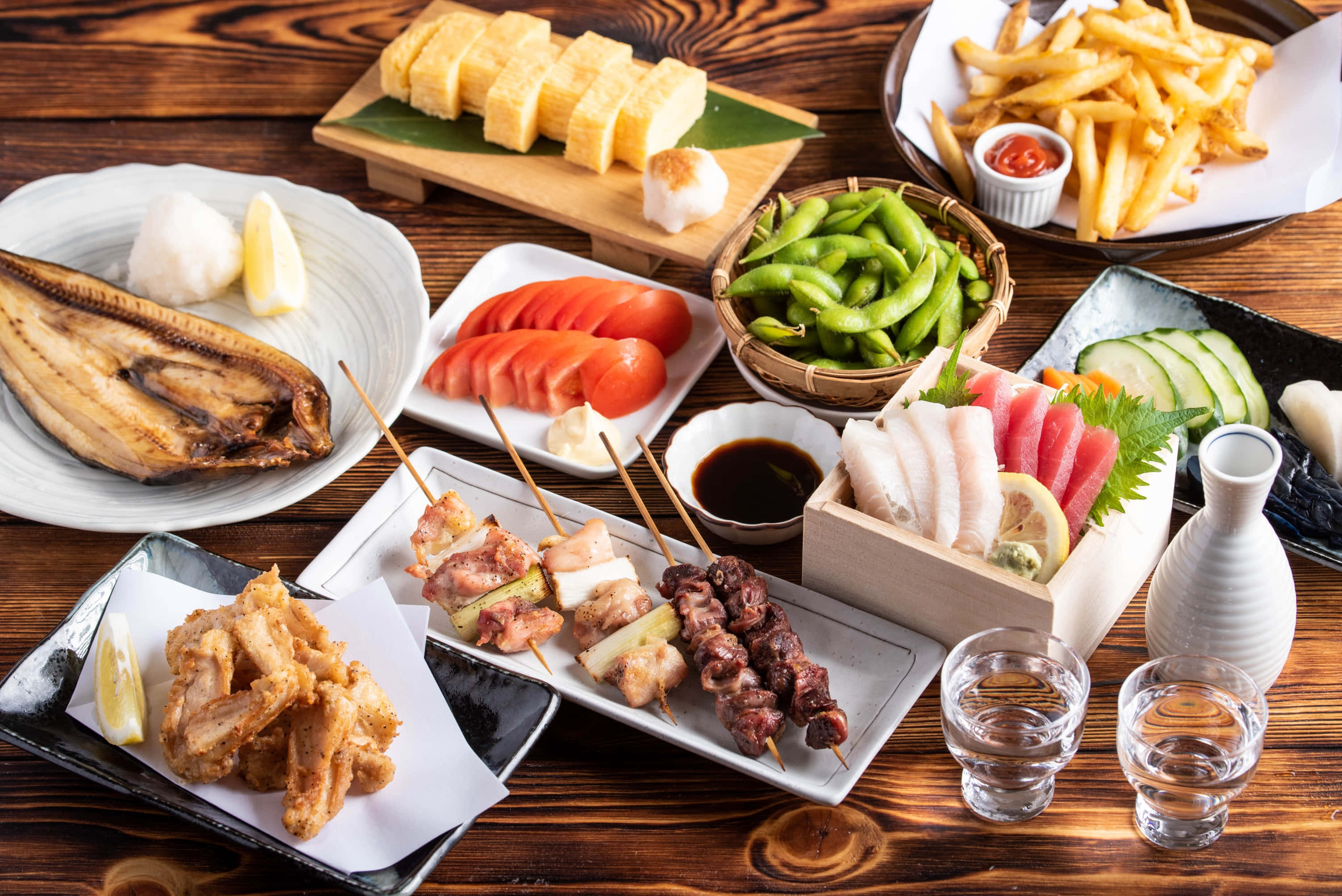 新鮮烹煮的填料彩椒 壁紙 — 豐盛的日本料理，包括烤魚、天婦羅、串燒、毛豆和壽司，擺放在質樸的木桌上。