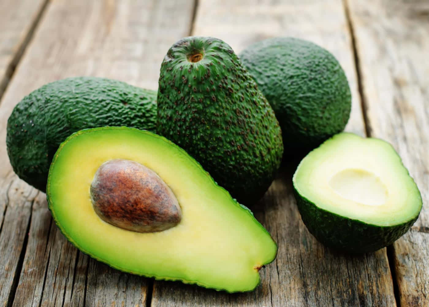 Avocado 桌布 壁紙 — 新鮮牛油果，其中一個切開一半，露出 creamy 果肉和果核，放在風化木板上。
