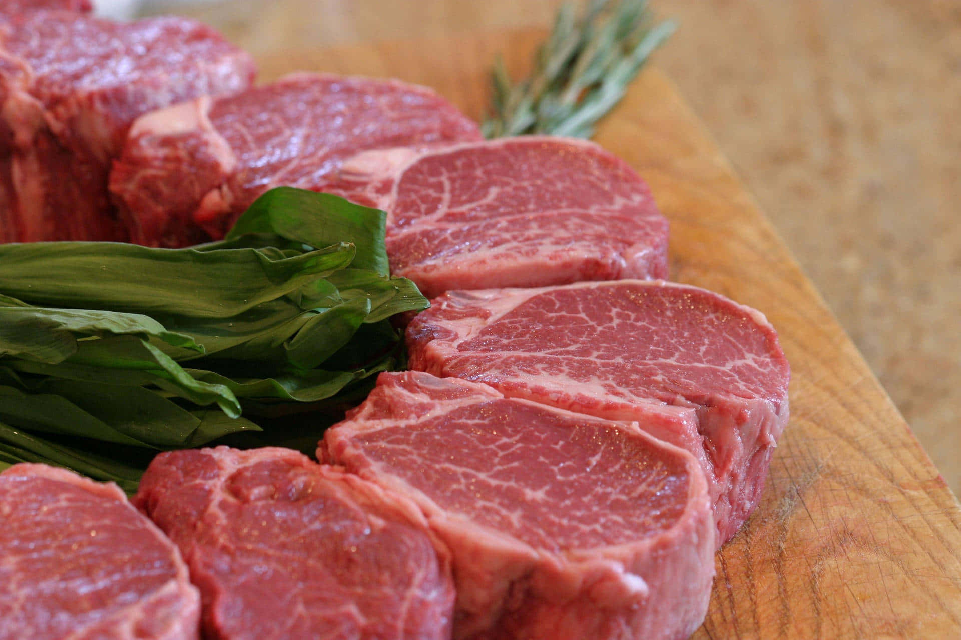 Red Meat 桌布 壁紙 — 新鮮生牛肉扒配綠色香草，擺放在木製砧板上。