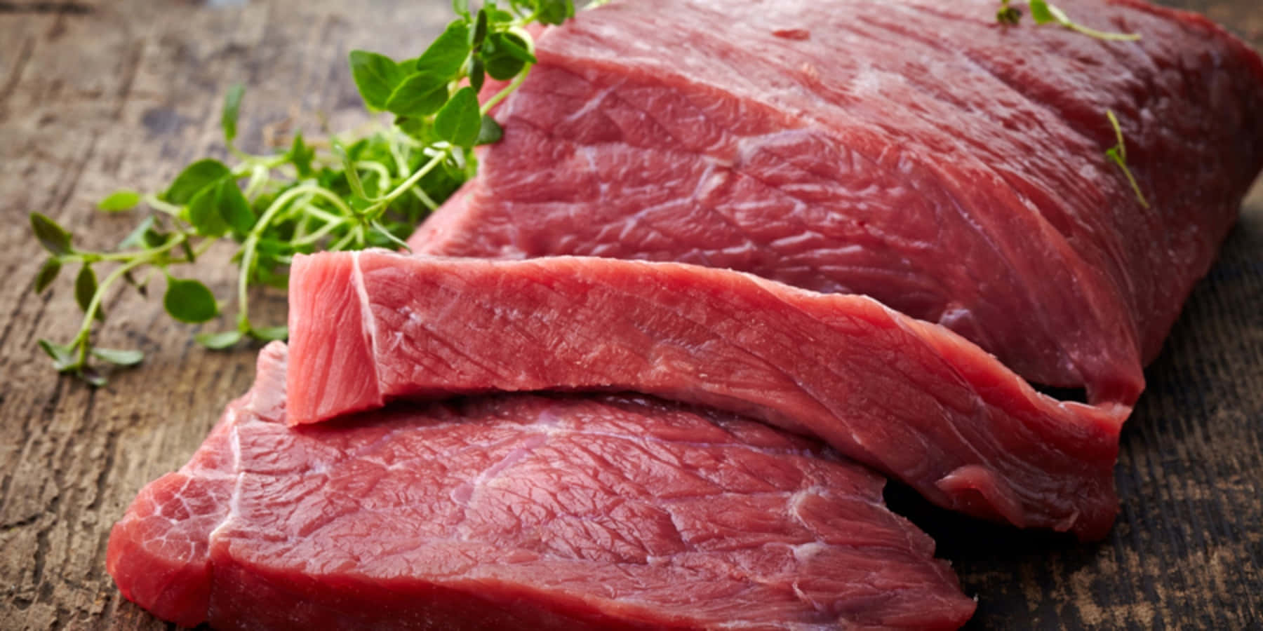 meat 桌布 壁紙 — 新鮮生牛肉扒配香草，置於質樸的木質表面上，展現豐富的紅色色調和自然質感。