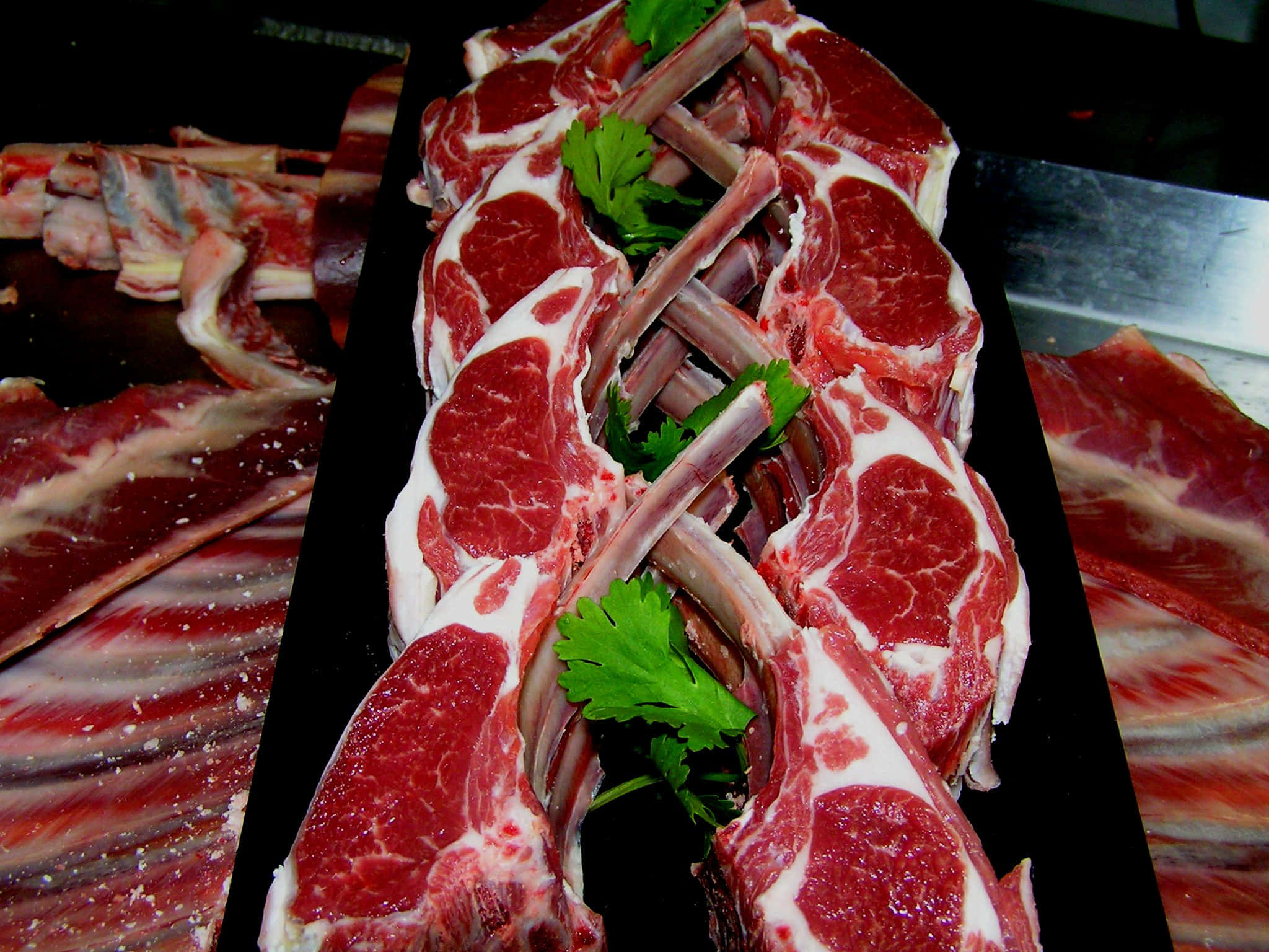 Red Meat 桌布 壁紙 — 新鮮生羊扒連骨，配以歐芹裝飾，排列在黑色托盤上，背景深色。
