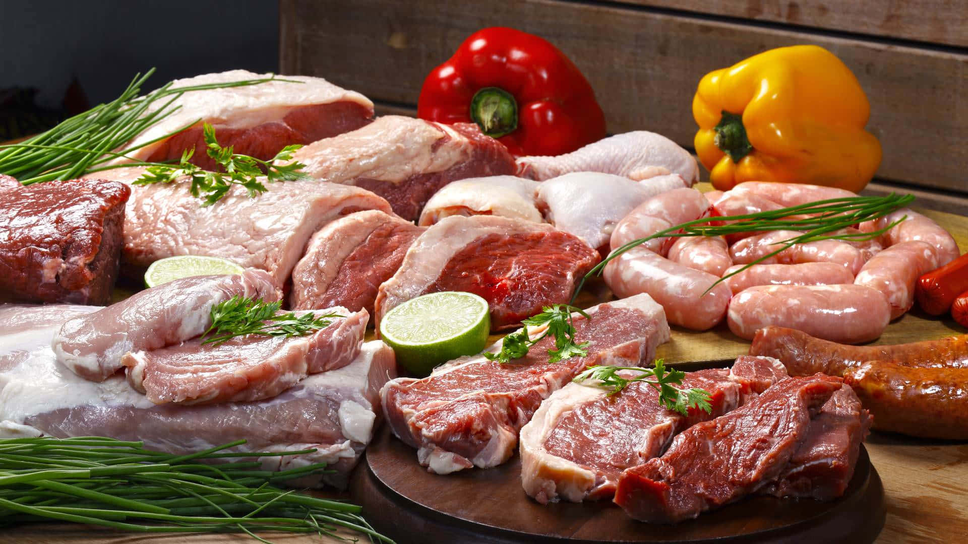 meat 桌布 壁紙 — 新鮮生肉包括牛扒、香腸和豬扒，與青檸片和彩色甜椒一起擺放在木板上。