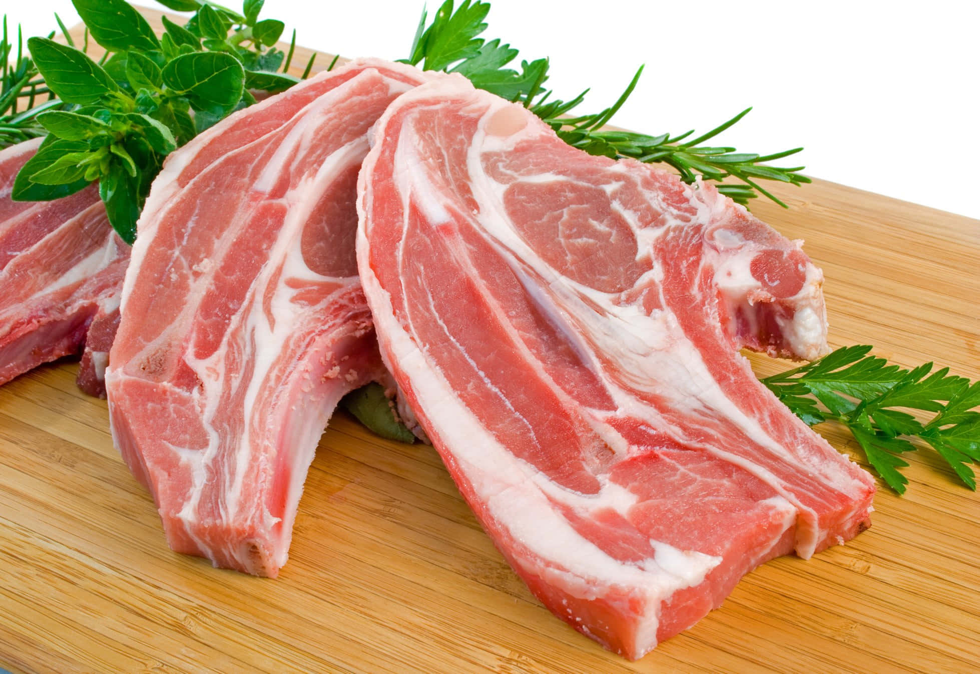 Red Meat 桌布 壁紙 — 新鮮生豬扒帶有大理石紋，放在木製砧板上，並以迷迭香和歐芹裝飾。