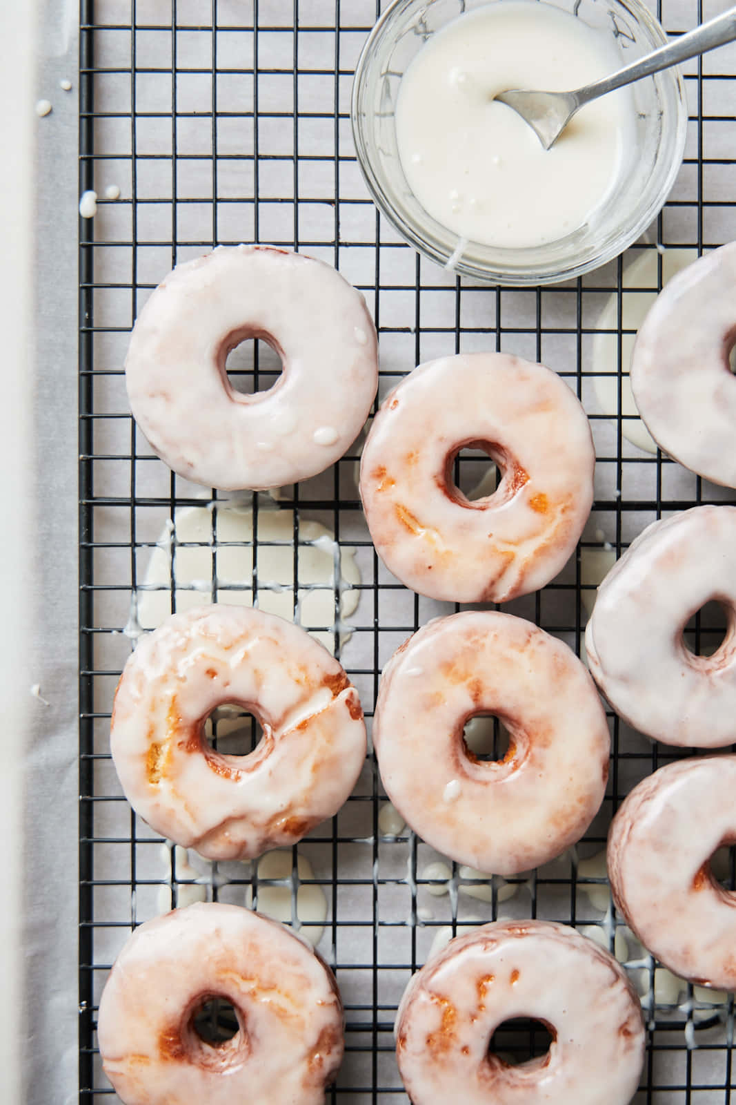 Glazed Donut 桌布 壁紙 — 新鮮的糖霜甜甜圈放在黑色金屬架上，旁邊有一碗白色糖霜和一個勺子。