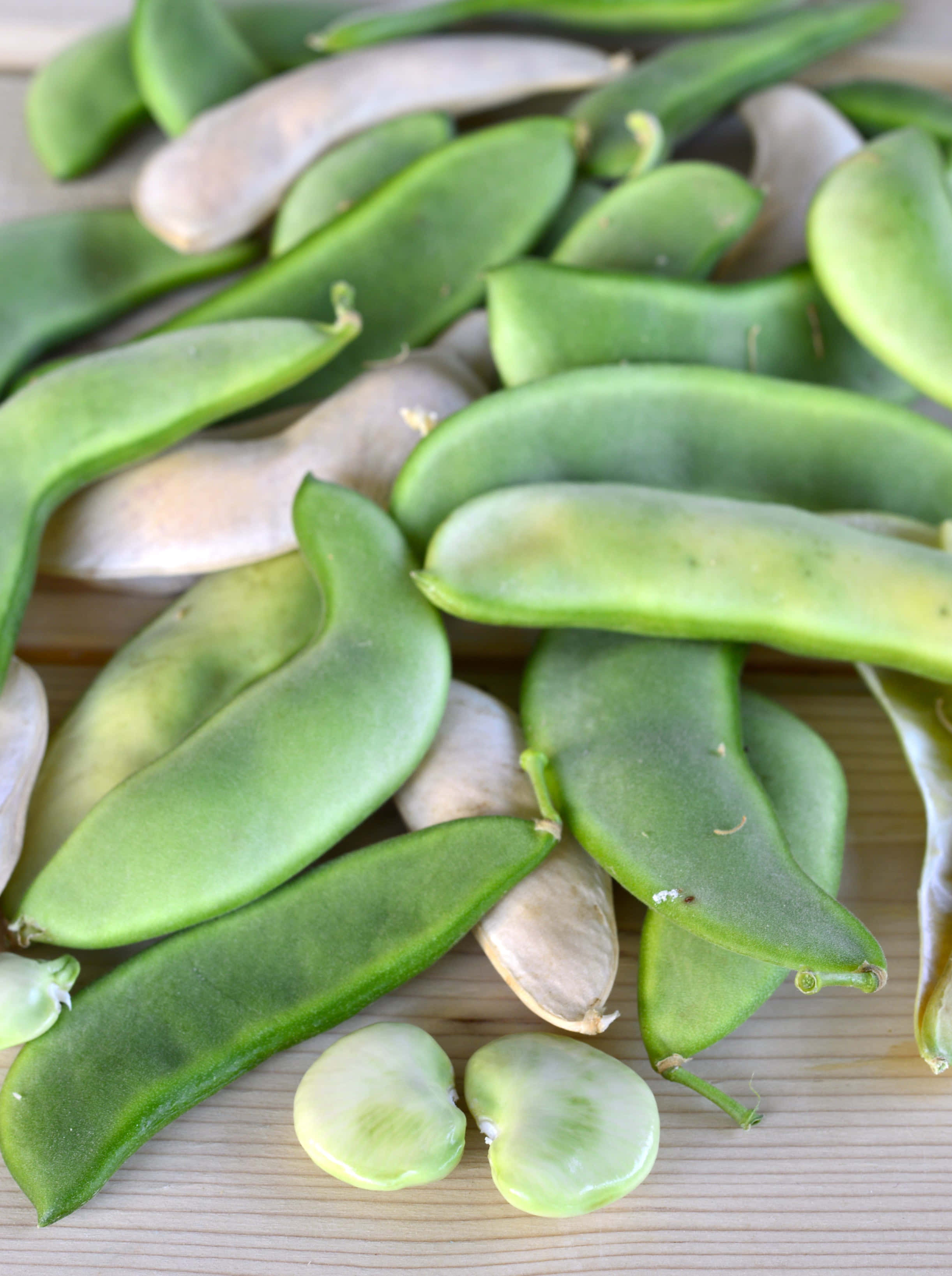 beans 桌布 壁紙 — 新鮮的綠色蠶豆莢和分開的豆子放在帶有自然紋理的淺色木質表面上。