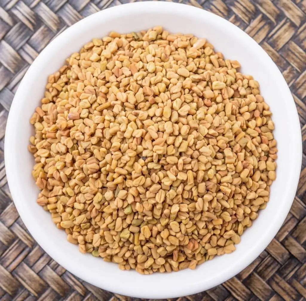 新鮮的茴香籽碗 壁紙 — 一個白色碗裝滿金色葫蘆巴籽，放在編織的棕色墊子上，俯視圖。