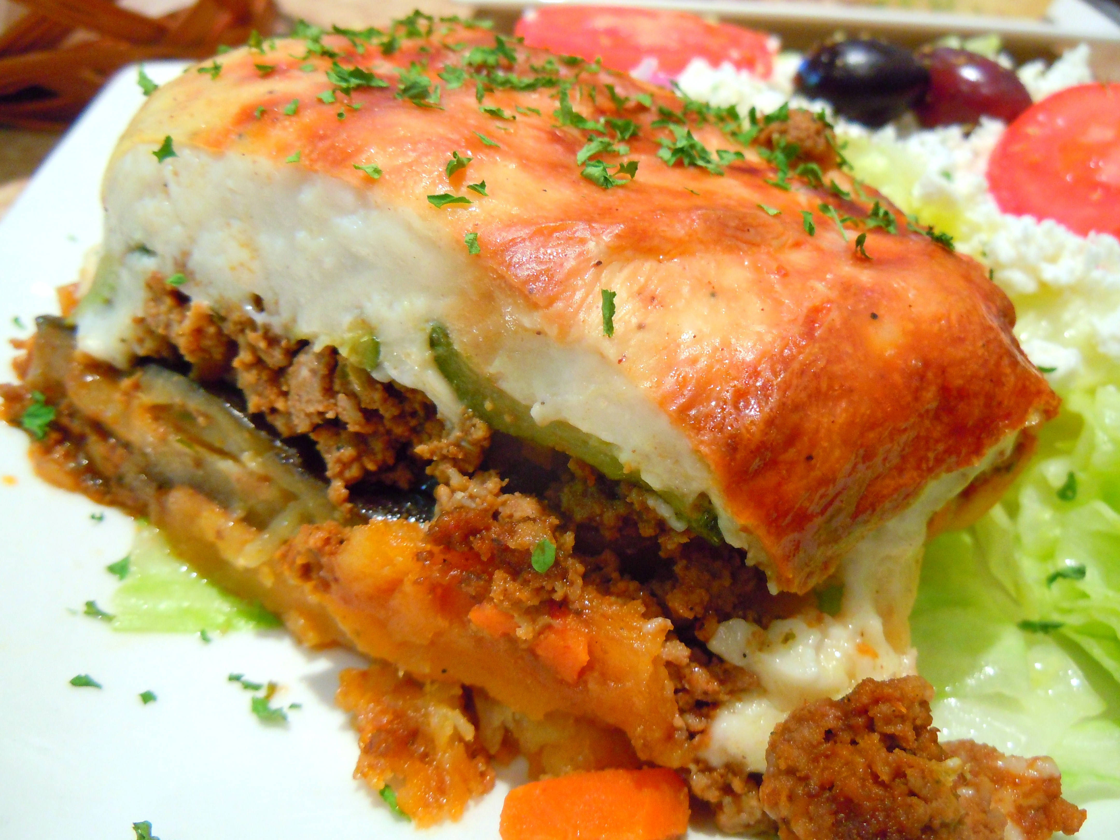 新鮮穆薩卡份量 壁紙 — 金黃色分層的慕薩卡，配上融化芝士和香草，放在生菜和番茄床上。