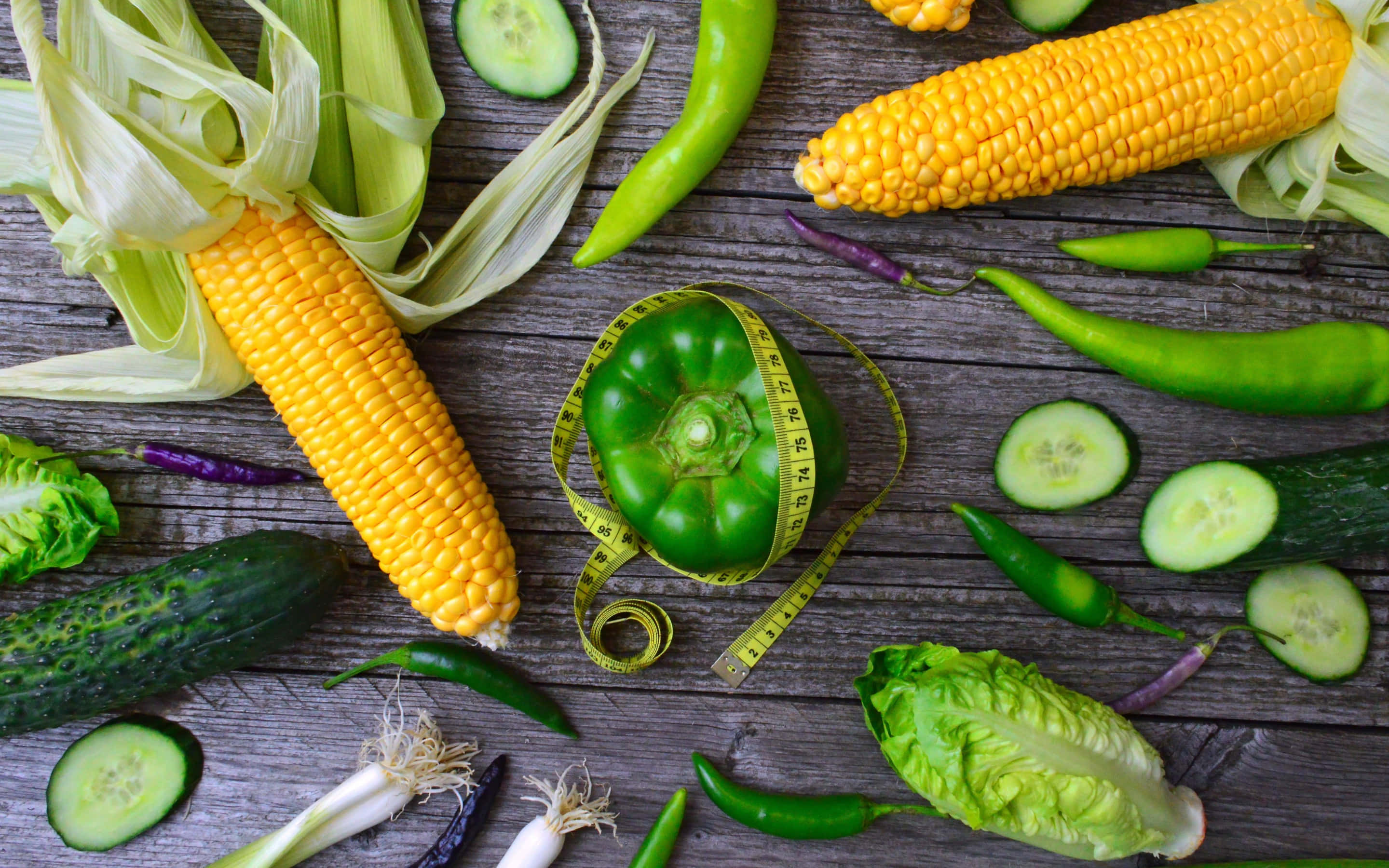 Corn 桌布 壁紙 — 新鮮粟米、青瓜和甜椒擺放在經風化的木頭上，綠色甜椒上纏繞著軟尺。