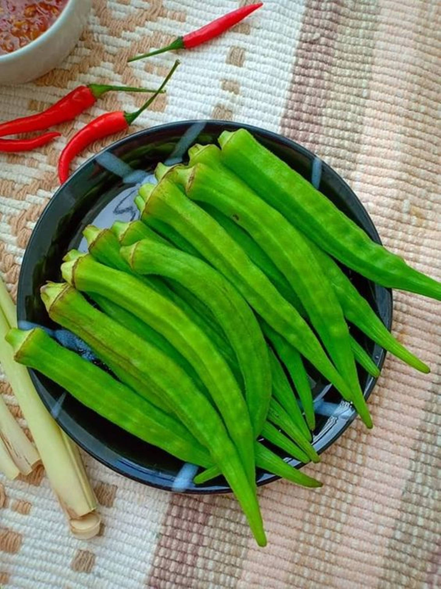 新鮮秋葵、辣椒和香茅排列在編織墊上備用烹調。