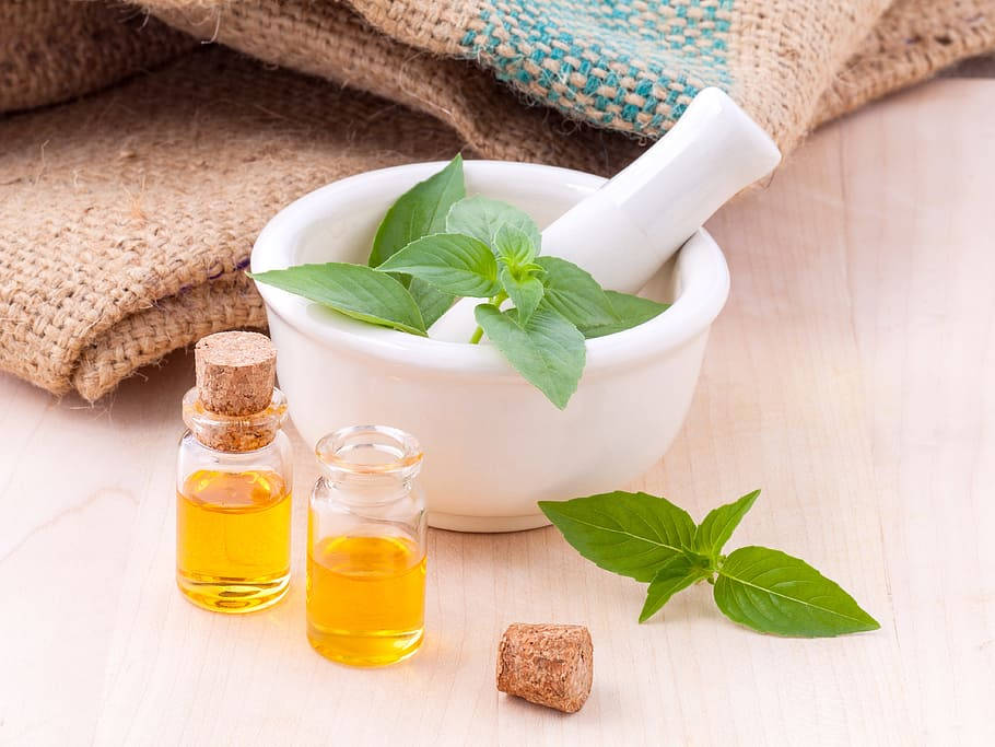 Healing 桌布 壁紙 — 新鮮羅勒葉放在白色研缽中，旁邊有細小的玻璃瓶裝著金色精油，置於淺色木質表面上。