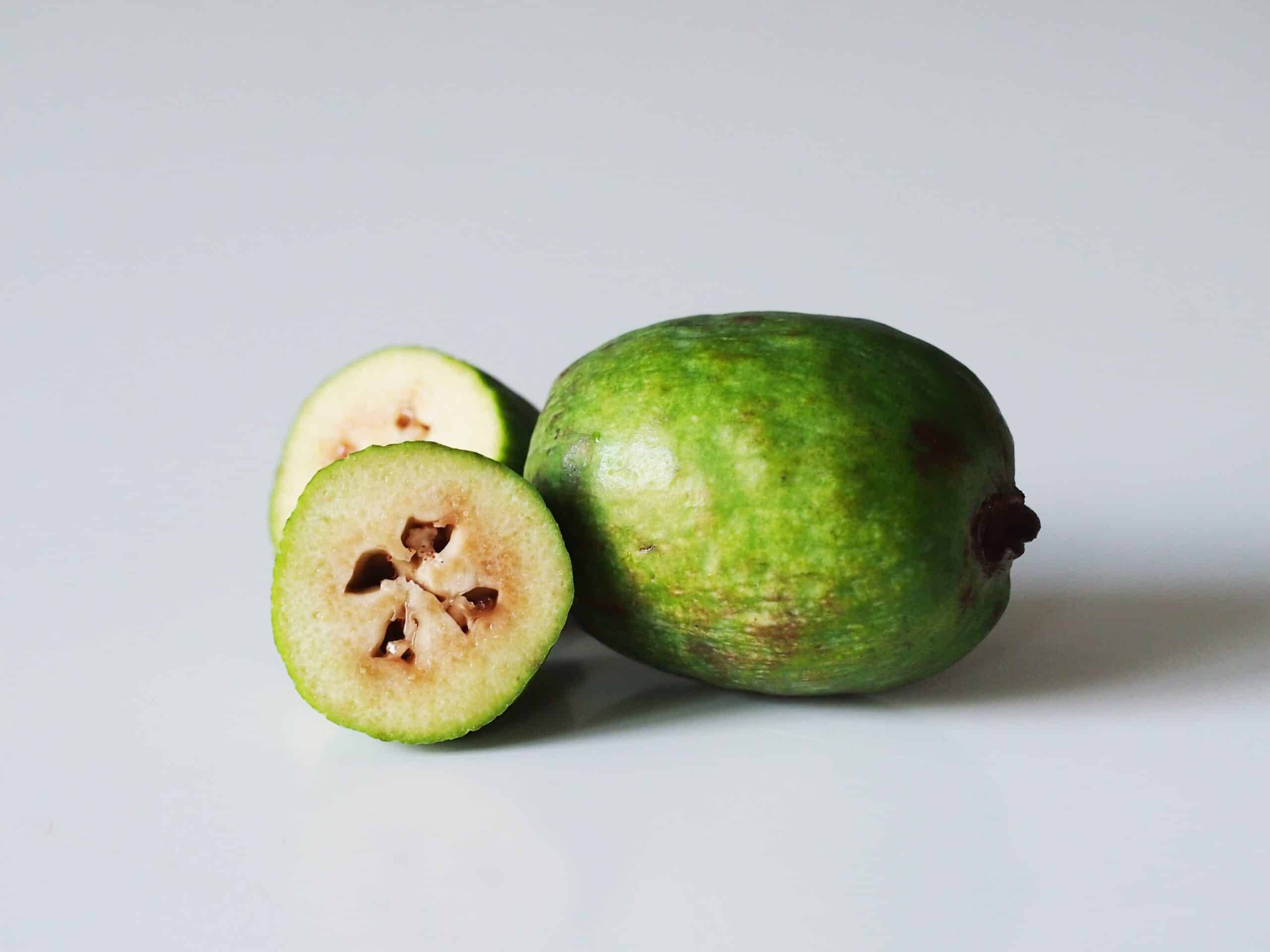 新鮮美味的番石榴——整顆與切半 壁紙 — 一個完整的綠色菲油果及其橫切面，在潔白表面上顯露出星形種子。