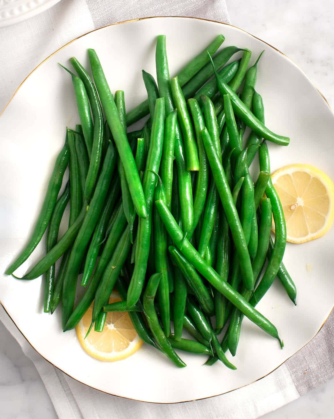 beans 桌布 壁紙 — 新鮮翠綠的四季豆高高堆放在白色碟子上，配上檸檬片和大理石背景。