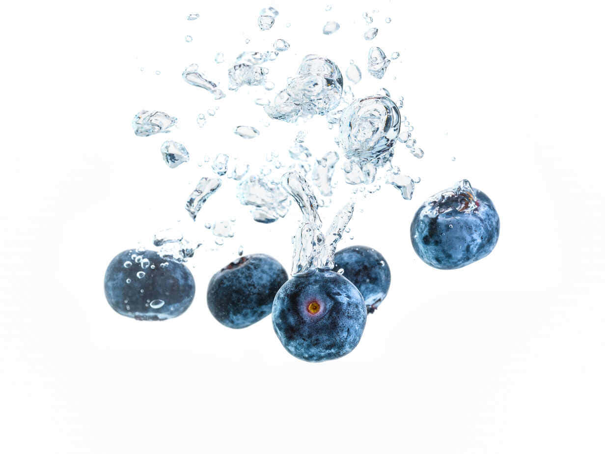Blueberry 桌布 壁紙 — 新鮮藍莓在清澈的水中戲劇性地飛濺，在純白背景上形成動態的氣泡和水滴。