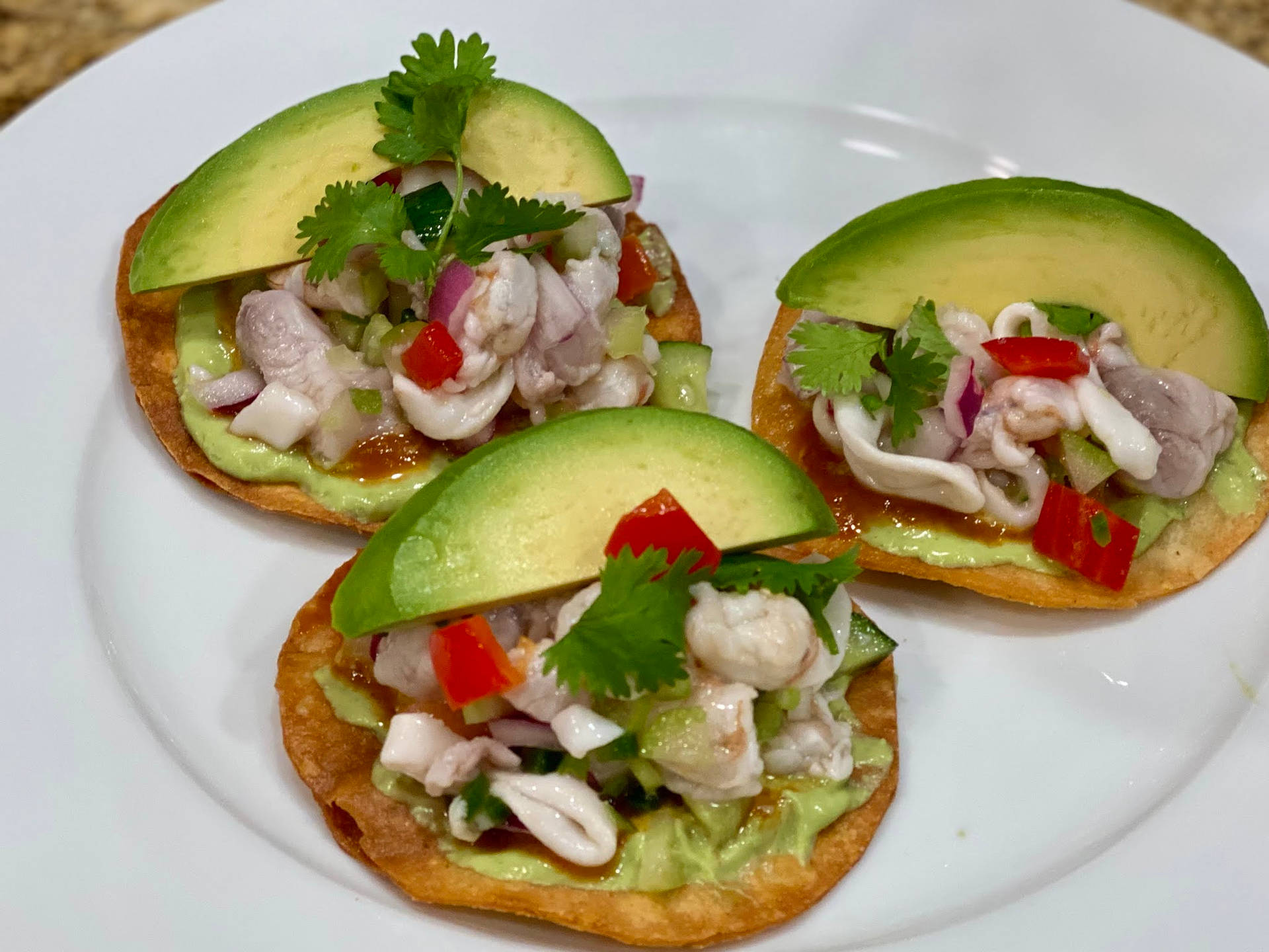 三個酸橘汁醃魚墨西哥脆餅，上面放上牛油果和芫荽，放在白色碟子上。