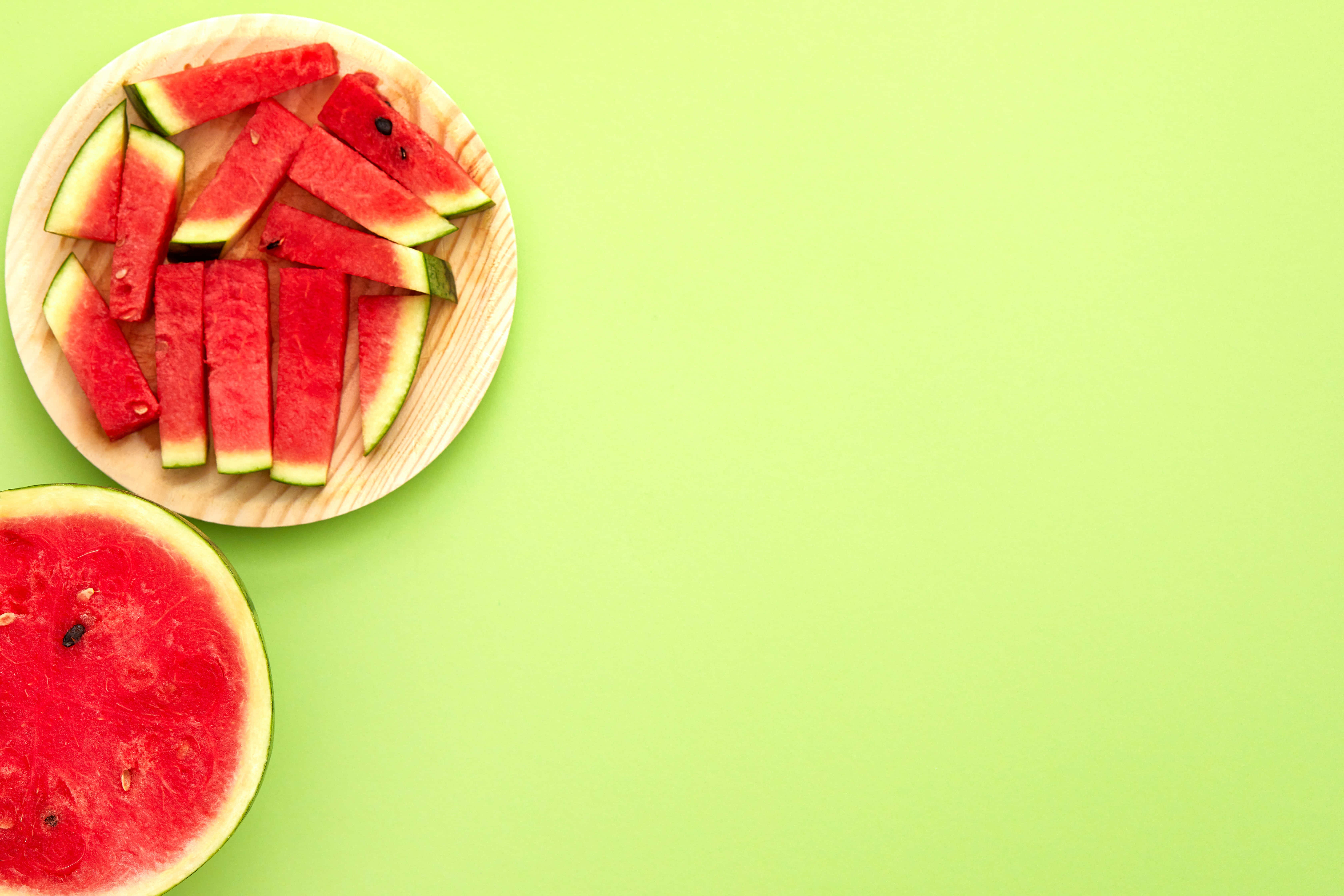 Summer Fruits 桌布 壁紙 — 新鮮西瓜片排列在木盤上，旁邊是半個切開的西瓜，背景係充滿活力嘅綠色。