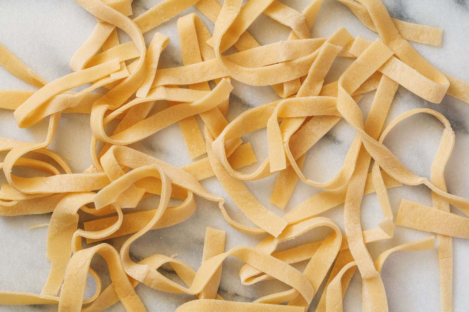 Noodles 桌布 壁紙 — 新鮮金黃色意粉絲帶散落在清涼的大理石表面上，柔和自然光線下。