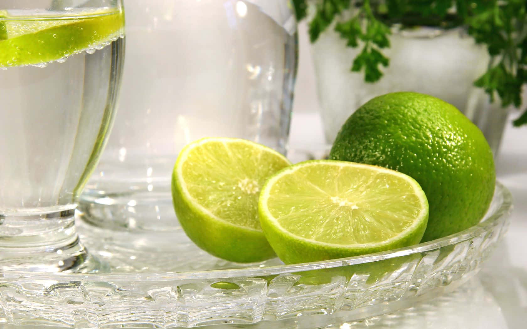 Lime 桌布 壁紙 — 新鮮青檸片和整個青檸放在水晶托盤上，旁邊有一杯加了青檸角的水。