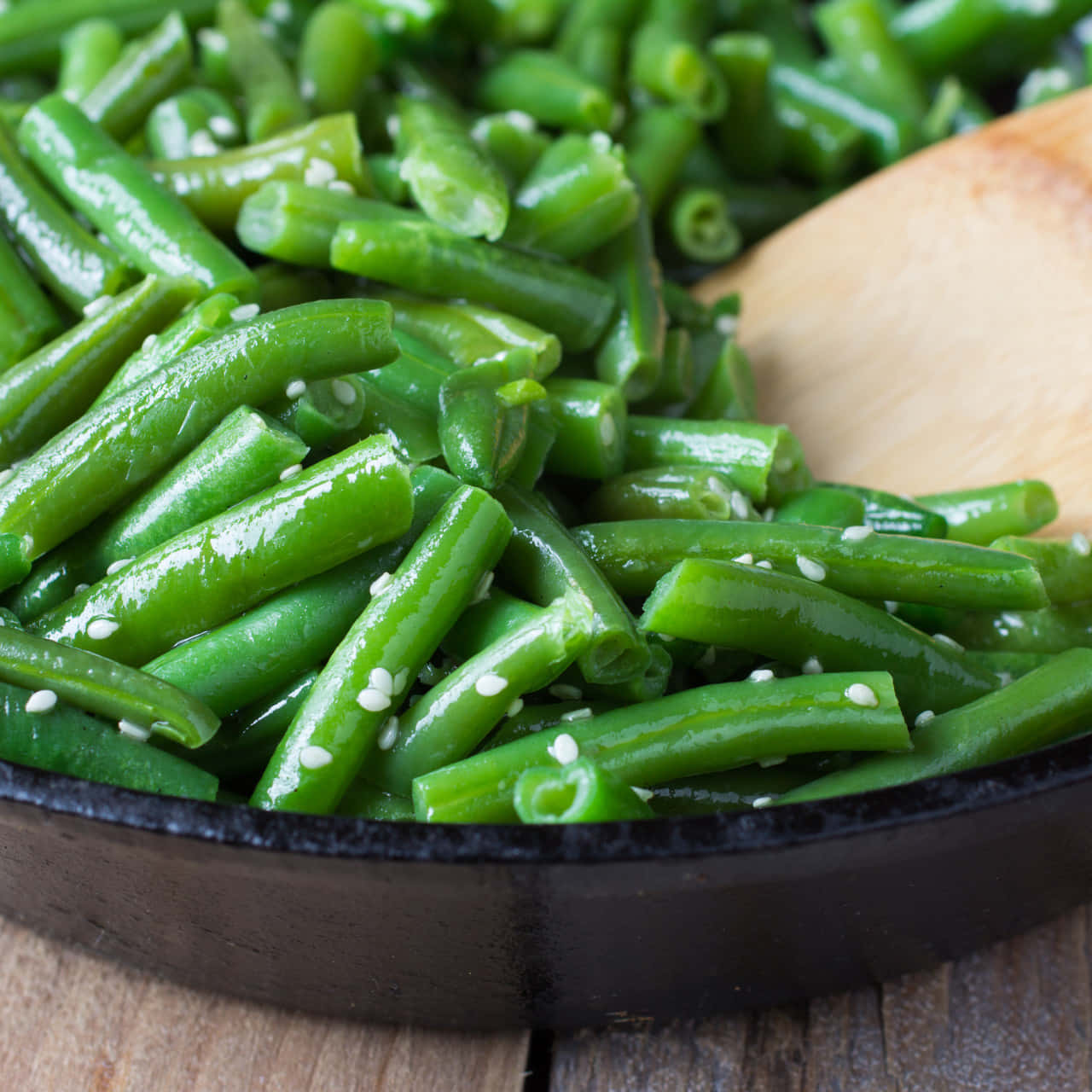 beans 桌布 壁紙 — 新鮮青豆在黑色平底鍋中閃爍著油光和芝麻，置於木質表面上。