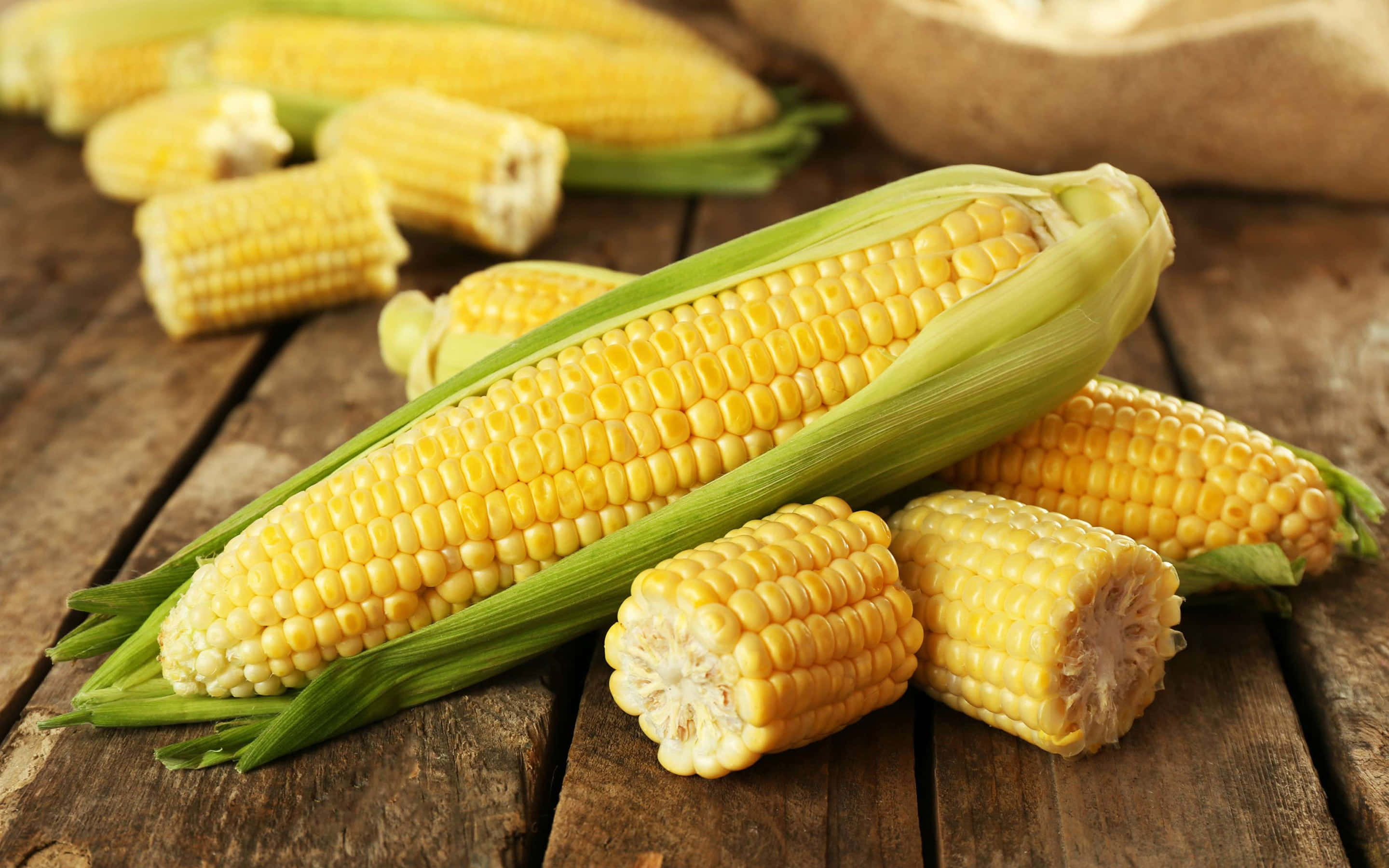 Yellow Corn 桌布 壁紙 — 新鮮黃色粟米連綠色外殼放在質樸的木桌上。
