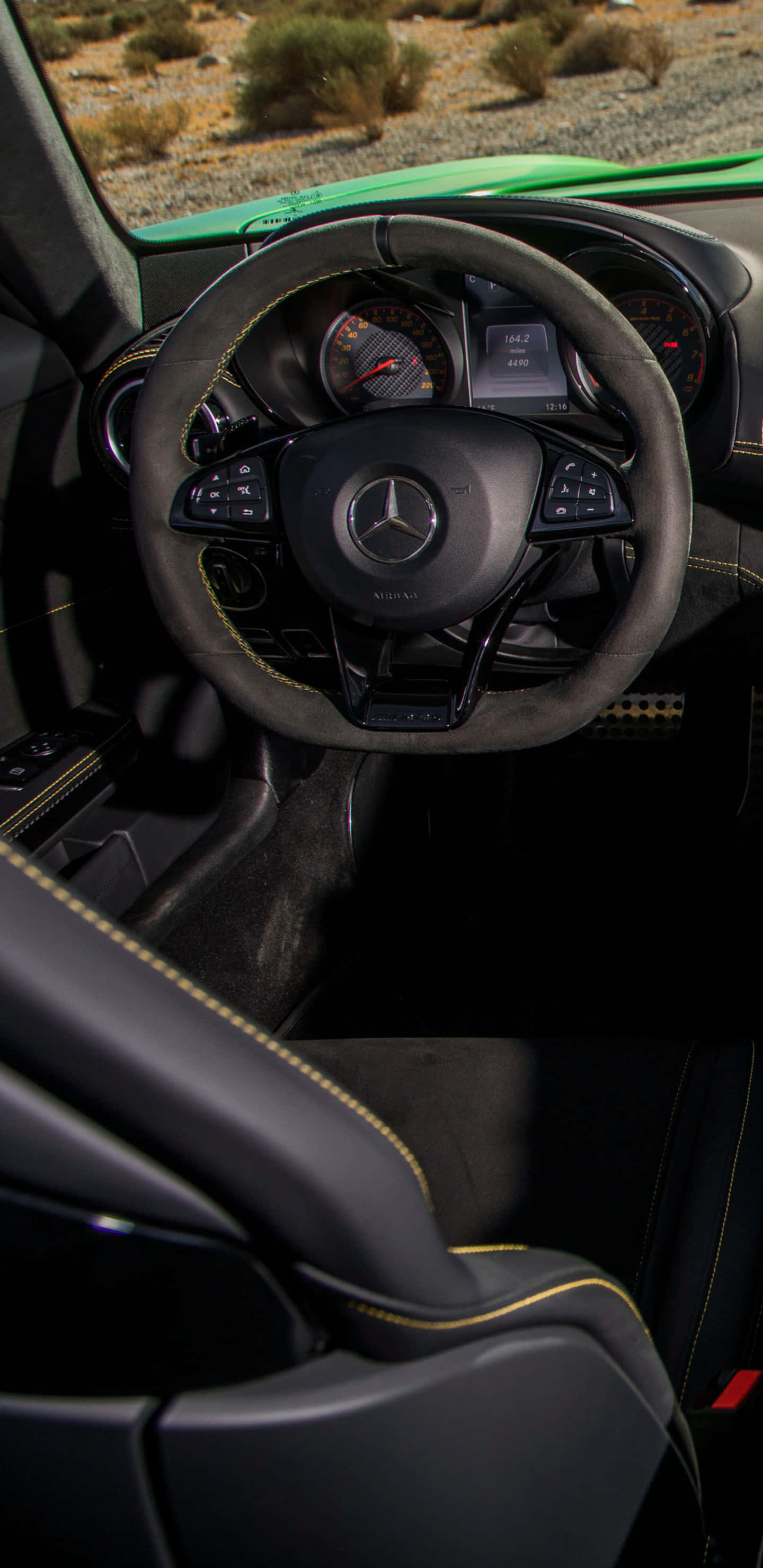 方向盤特寫 Pixel 3XL AMG GT-R 背景 壁紙 — 豪華汽車內部特寫，黑色皮革座椅配黃色縫線，從駕駛座視角望向沙漠背景。