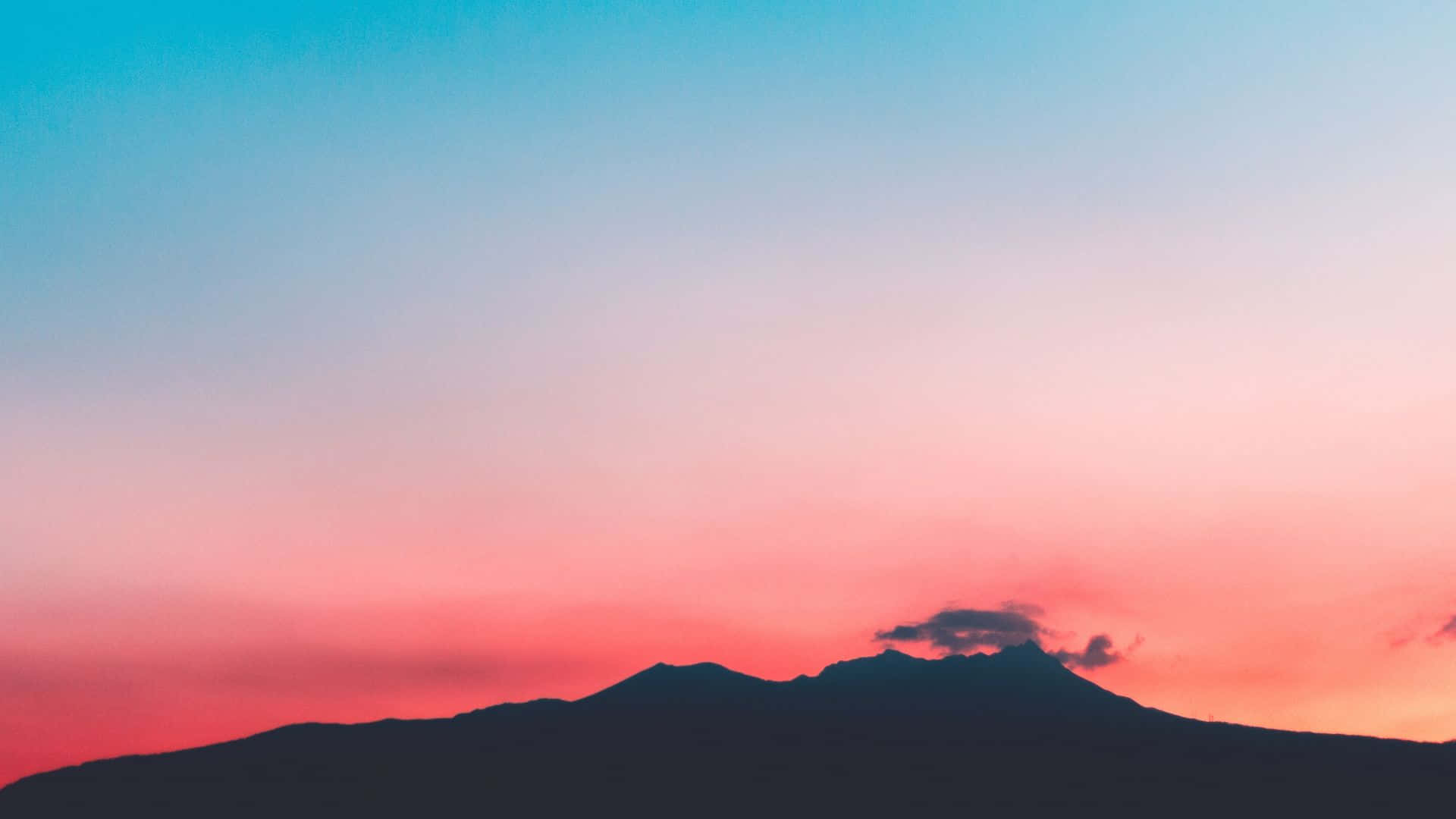 旅人被日落天空的美景深深吸引 壁紙 — 山脈的剪影，映襯著充滿活力的粉紅色和藍色日落天空，伴隨著縷縷薄雲。