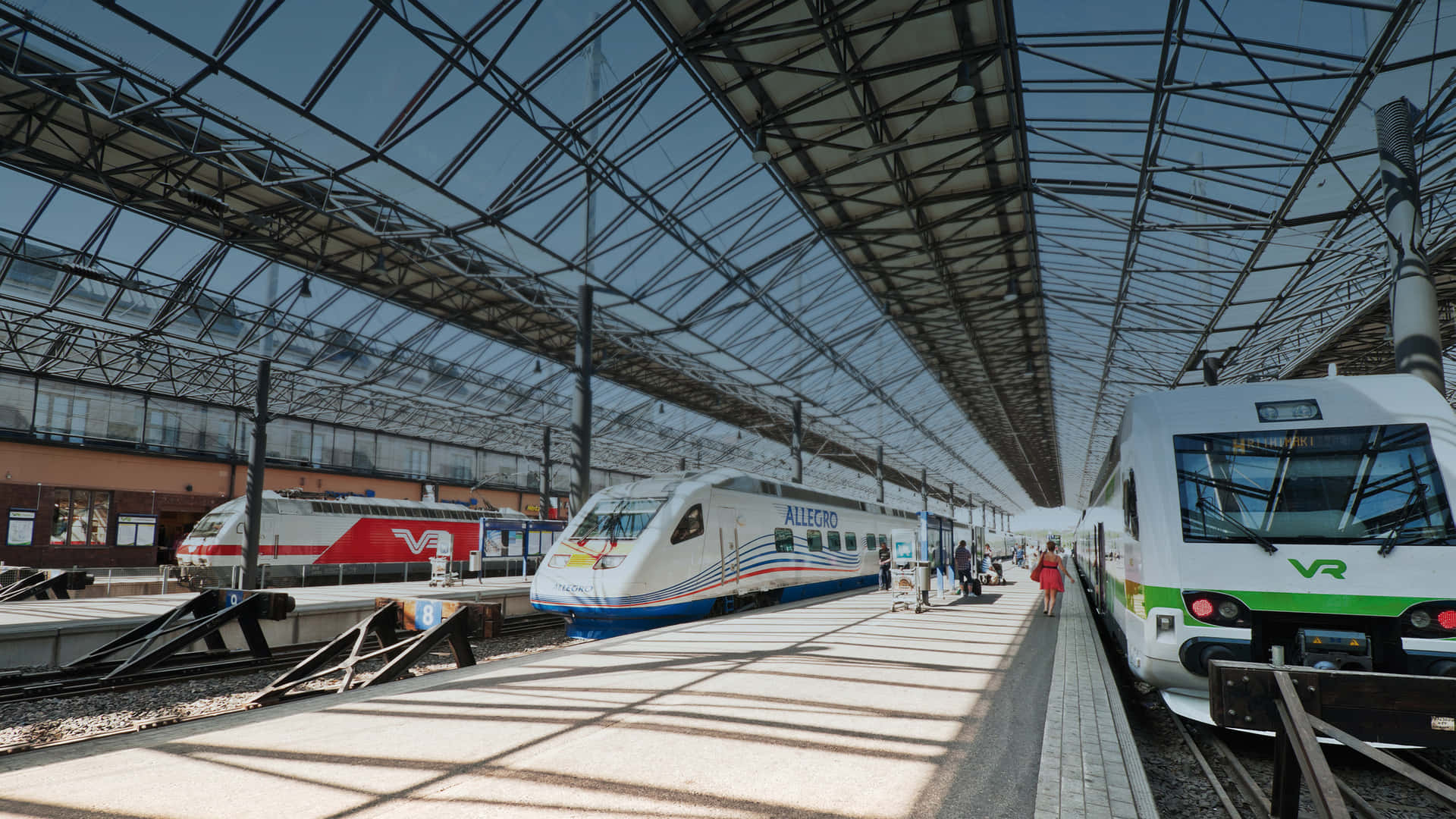 乘客在明亮的玻璃屋頂車站中，在流線型列車之間行走。