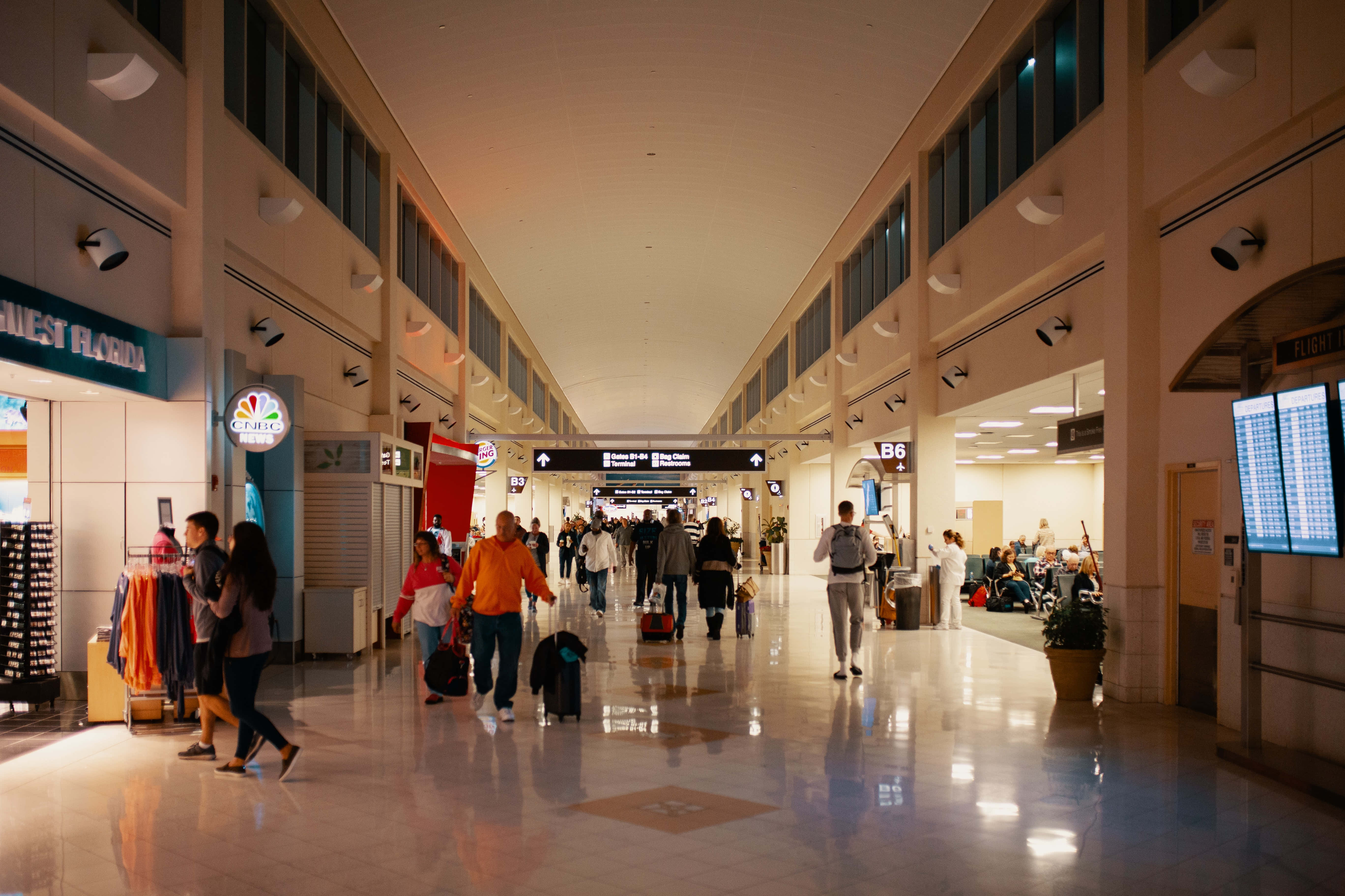 Airport 桌布 壁紙 — 旅客在光線明亮的機場客運大樓中穿梭，拋光地板和頭頂標誌引導他們穿過繁忙的空間。