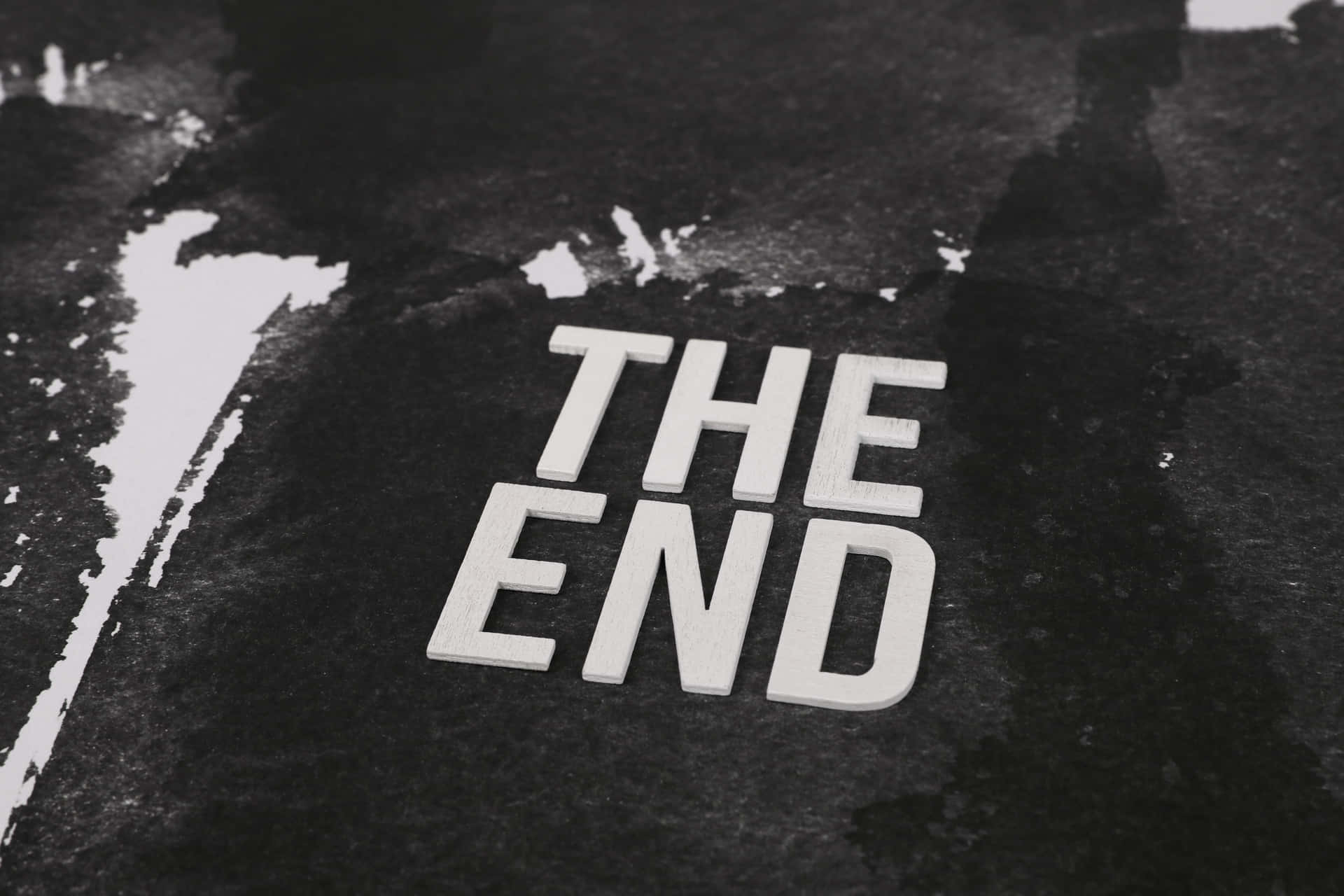 白色3D字母拼出'THE END'，在帶有油漆飛濺的深色紋理背景上。