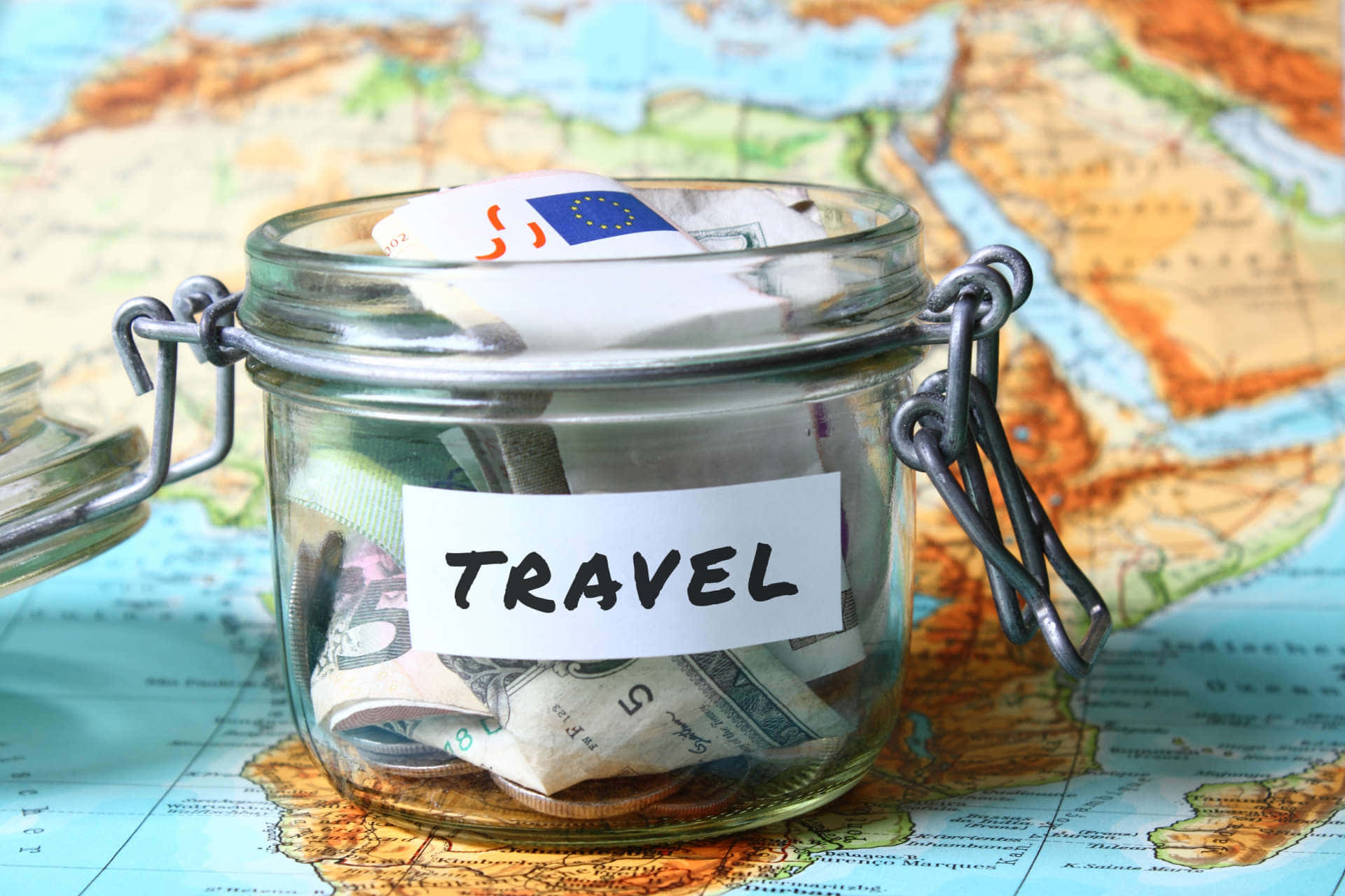 標有旅行的玻璃罐裝滿現金放在世界地圖上。
