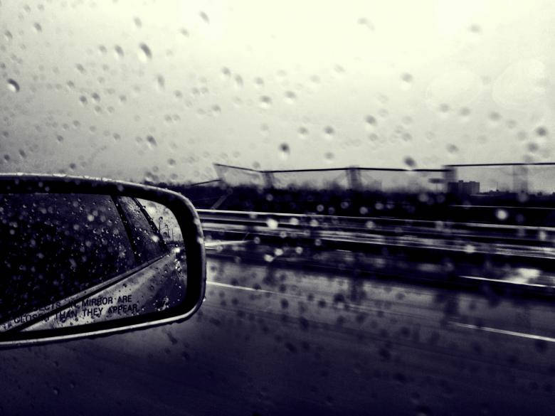 汽車側鏡在雨天反射高速公路，玻璃上有水滴。