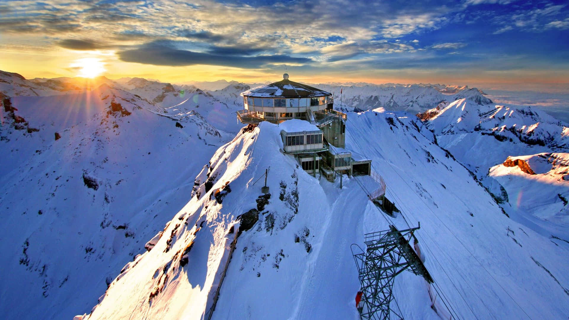 Switzerland 桌布 壁紙 — 日出時分，白雪覆蓋的山峰頂上有一座現代天文台，在無盡的高山地形上投下長長的陰影。