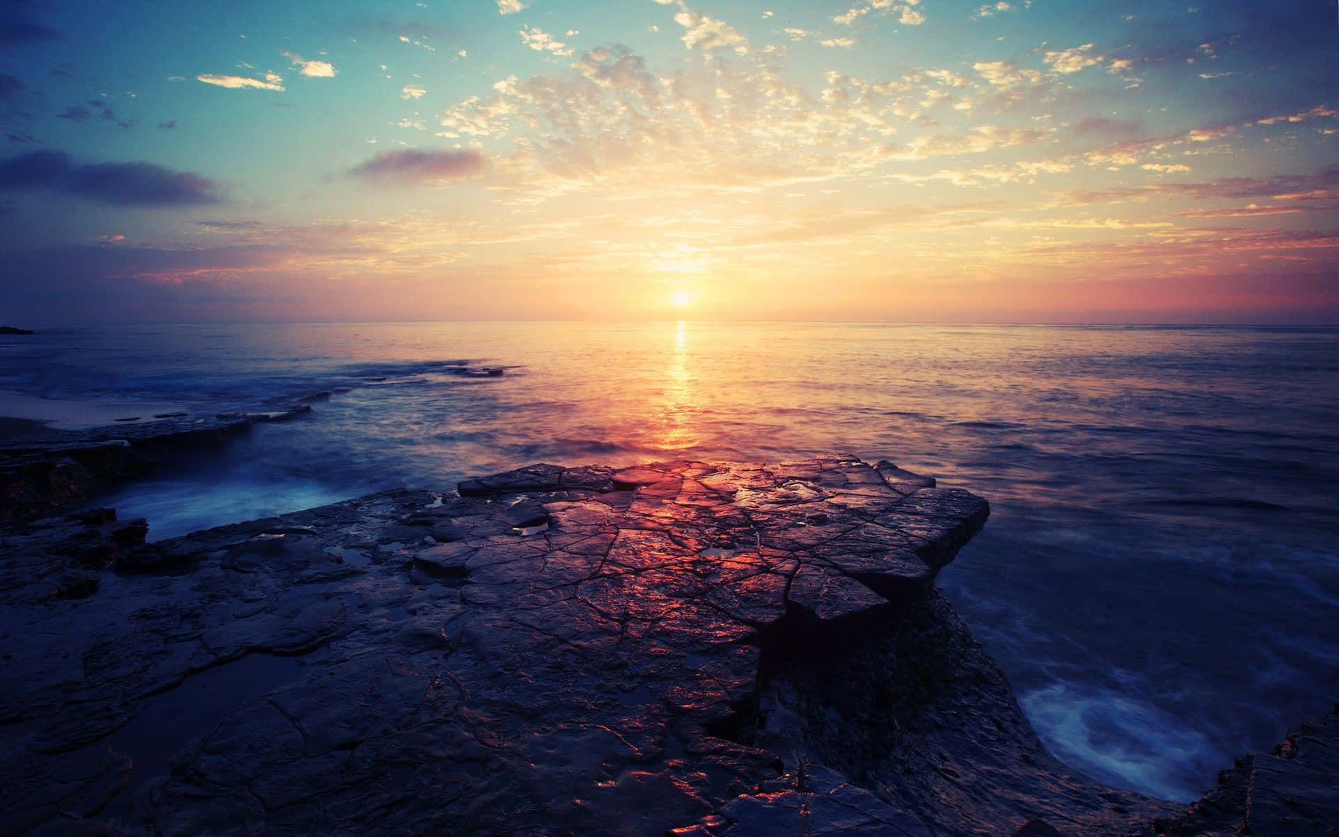 海洋上的夕陽，前景的岩石反射出溫暖的色彩。