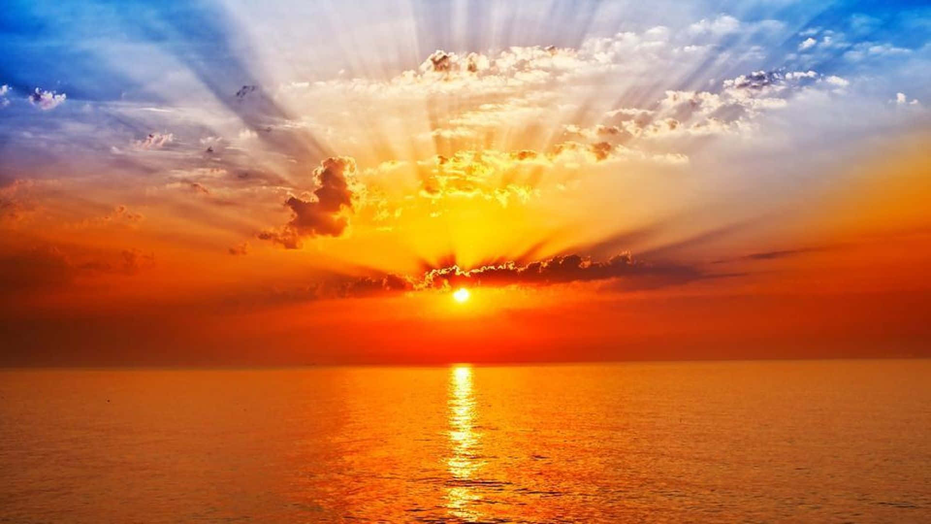 日出灑落寧靜湖面 壁紙 — 日落時分，陽光穿透雲層，照射在平靜的海面上，泛起金色的倒影。