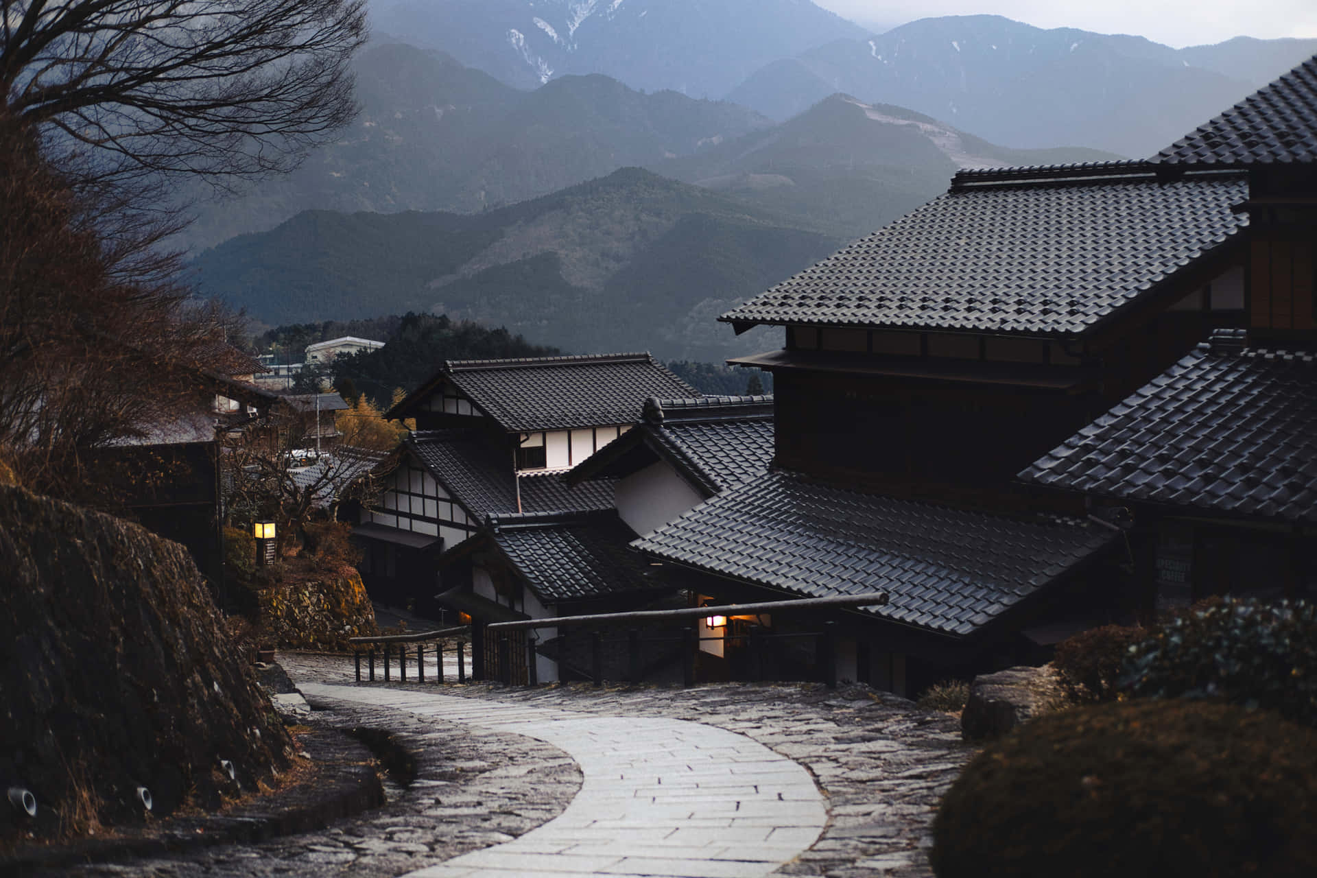 蜿蜒的石徑穿過傳統的日本村莊，背景是積雪的山峰。