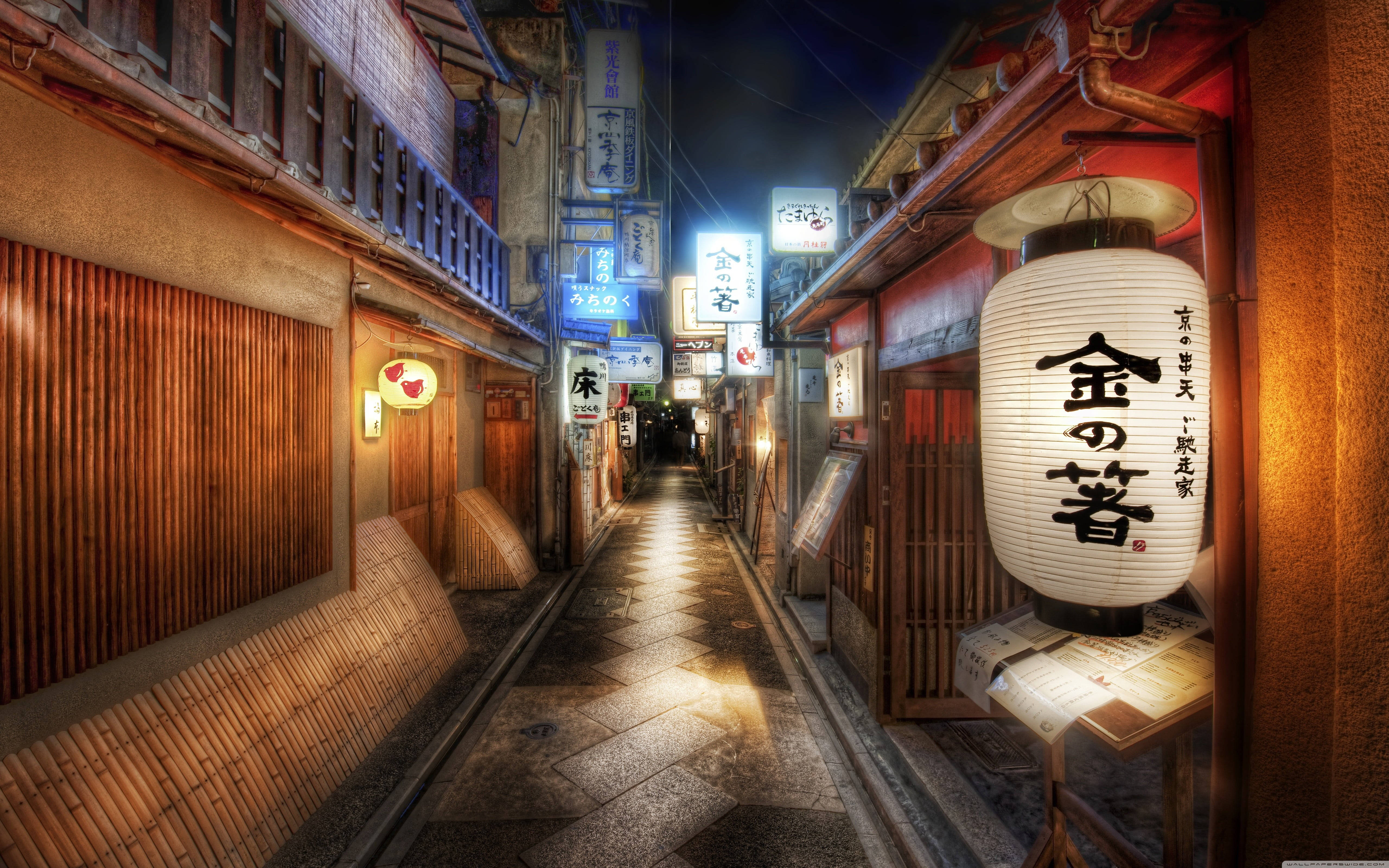 日式動漫京都小巷 壁紙 — 夜晚一條狹窄的日本小巷，被發光的燈籠和霓虹燈招牌照亮，倒映在濕漉漉的石板路上。
