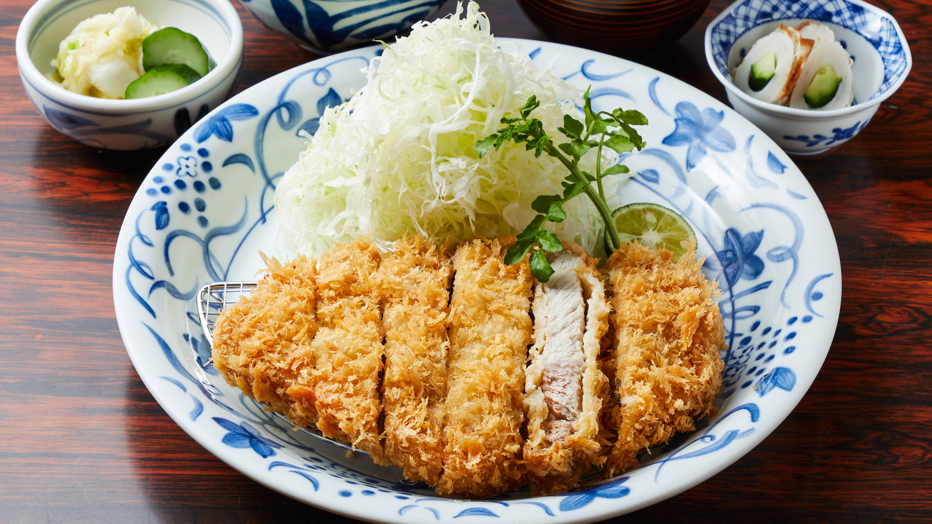 日式料理之樂 - 正宗豬排餐點 壁紙 — 金黃色切片炸豬排配椰菜絲和裝飾，放在藍色花卉碟上。