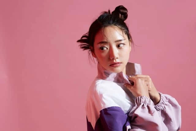 身穿紫色和白色外套的年輕女性在粉紅色背景前擺姿勢