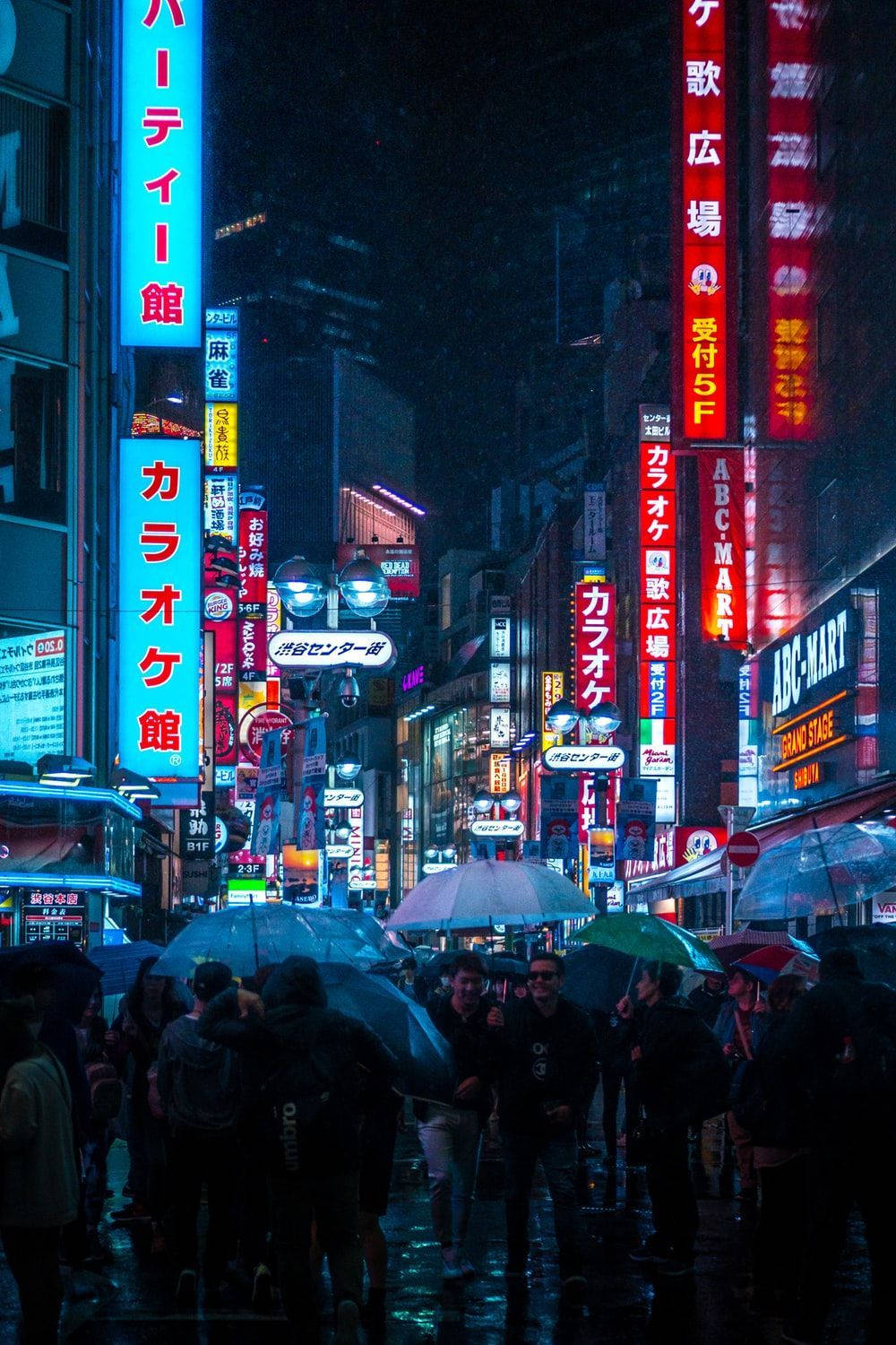 夜晚霓虹燈照亮的東京街道，人們在雨中撐傘。