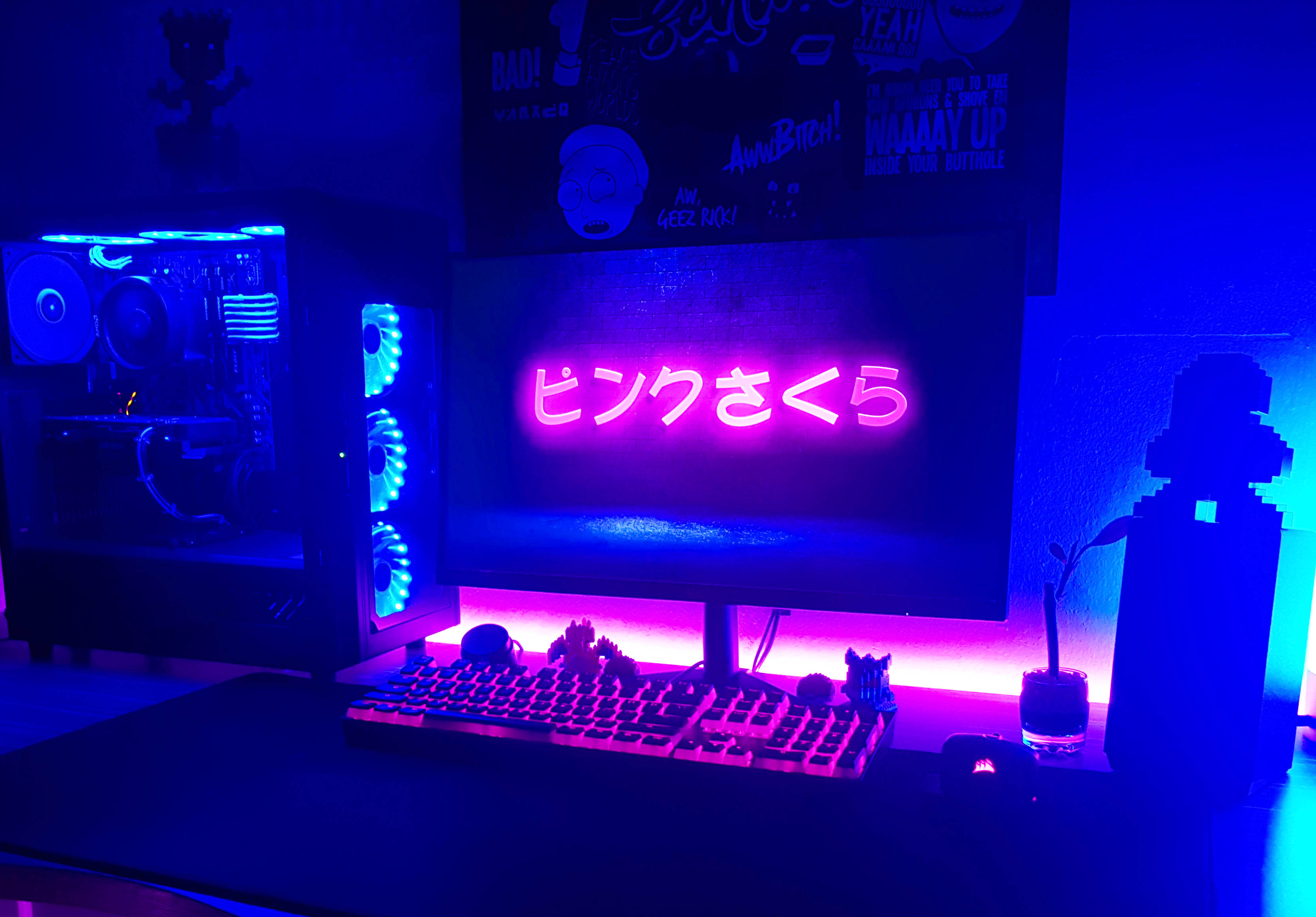 日式遊戲電腦 壁紙 — 一個發光的藍色和粉紅色遊戲設置，帶有霓虹燈日文文字屏幕和自訂PC機箱，在昏暗的房間中。