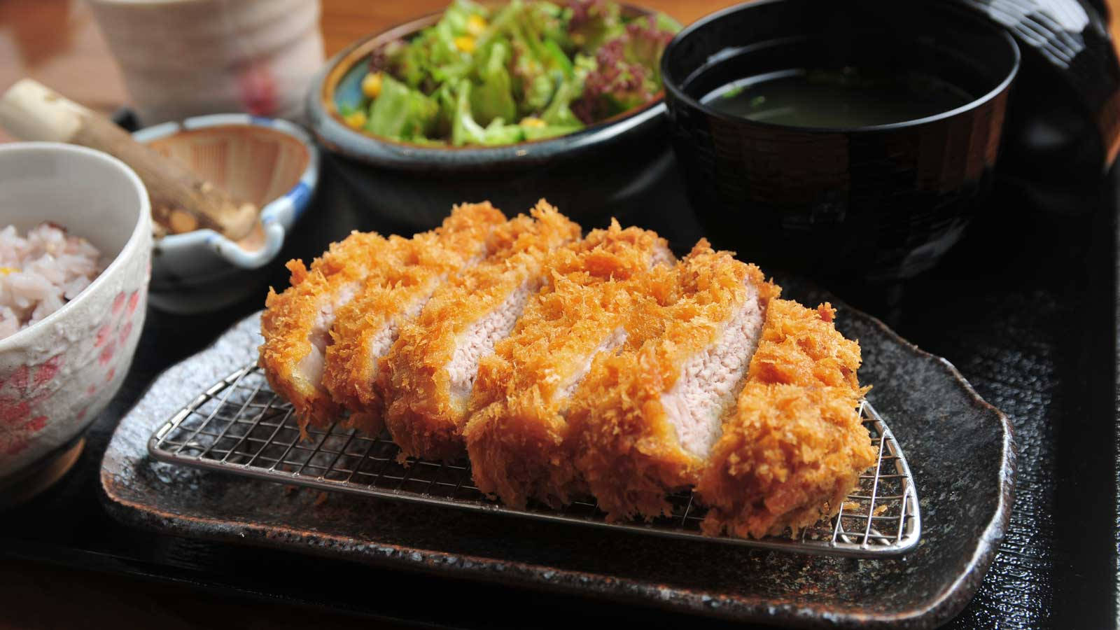 日式雞肉炸豬排切片 壁紙 — 金黃色切片吉列豬排放在金屬架上，配以米飯沙律和味噌湯，盛載於傳統日本碗中。