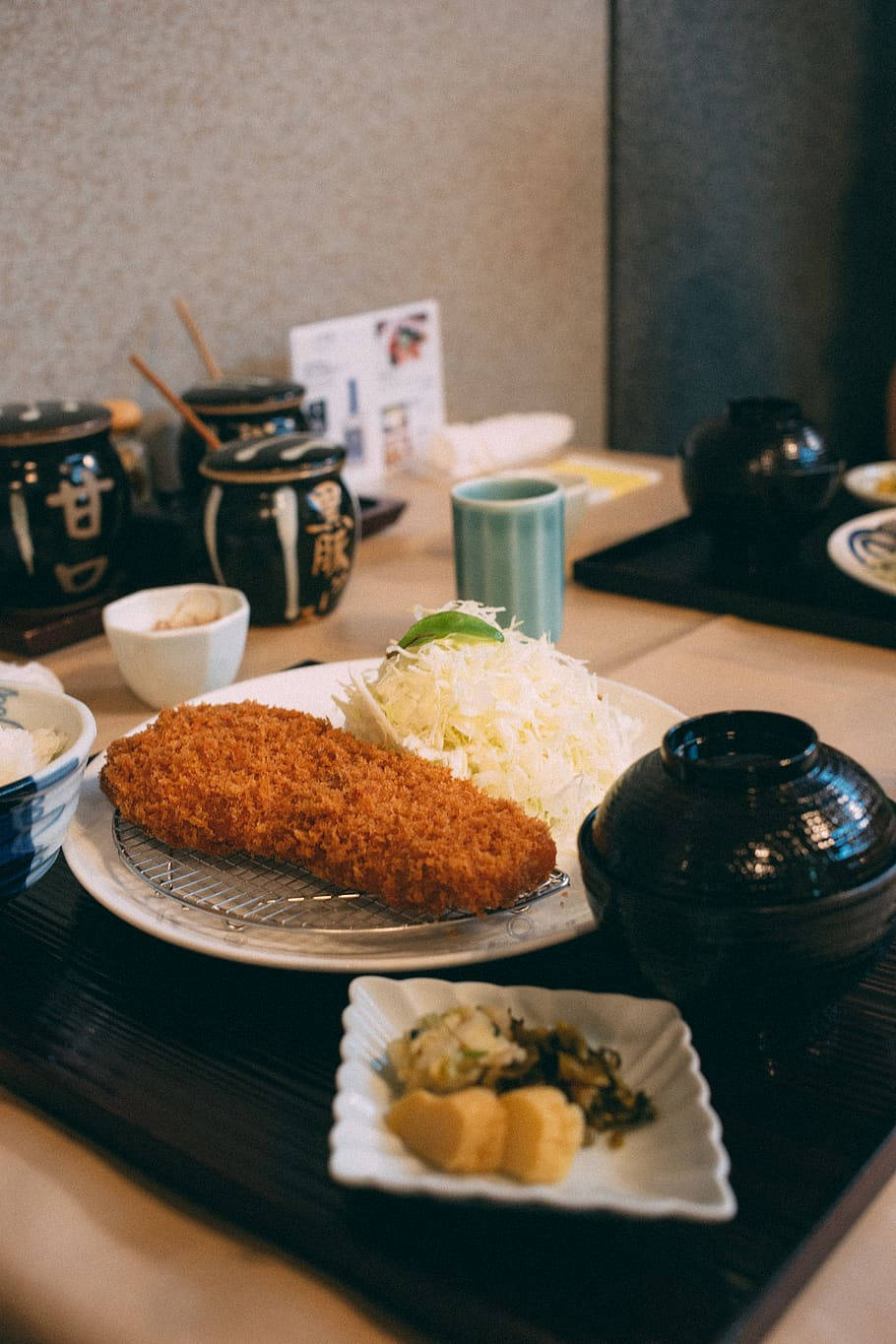 日式餐廳中的美味炸豬排 壁紙 — 金黃色的炸豬排配上椰菜絲和配菜，放在傳統日本餐廳的木托盤上。