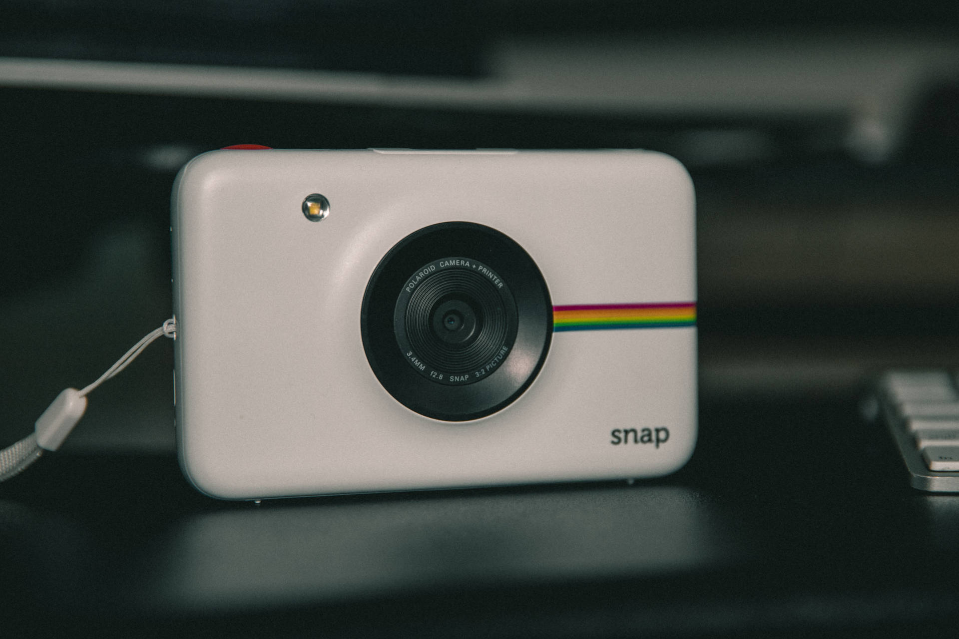 帶有彩虹條紋的白色Polaroid Snap相機，深色桌子上，旁邊有鍵盤。