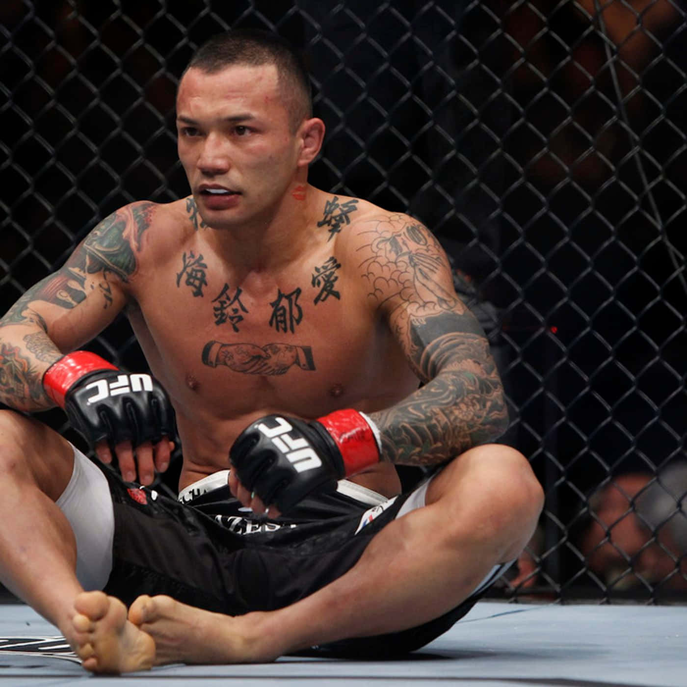 日本UFC戰士Norifumi 'Kid' Yamamoto沉思姿態 壁紙 — 一位有紋身的混合武術選手在比賽後戴著UFC手套筋疲力盡地坐在八角籠地上。